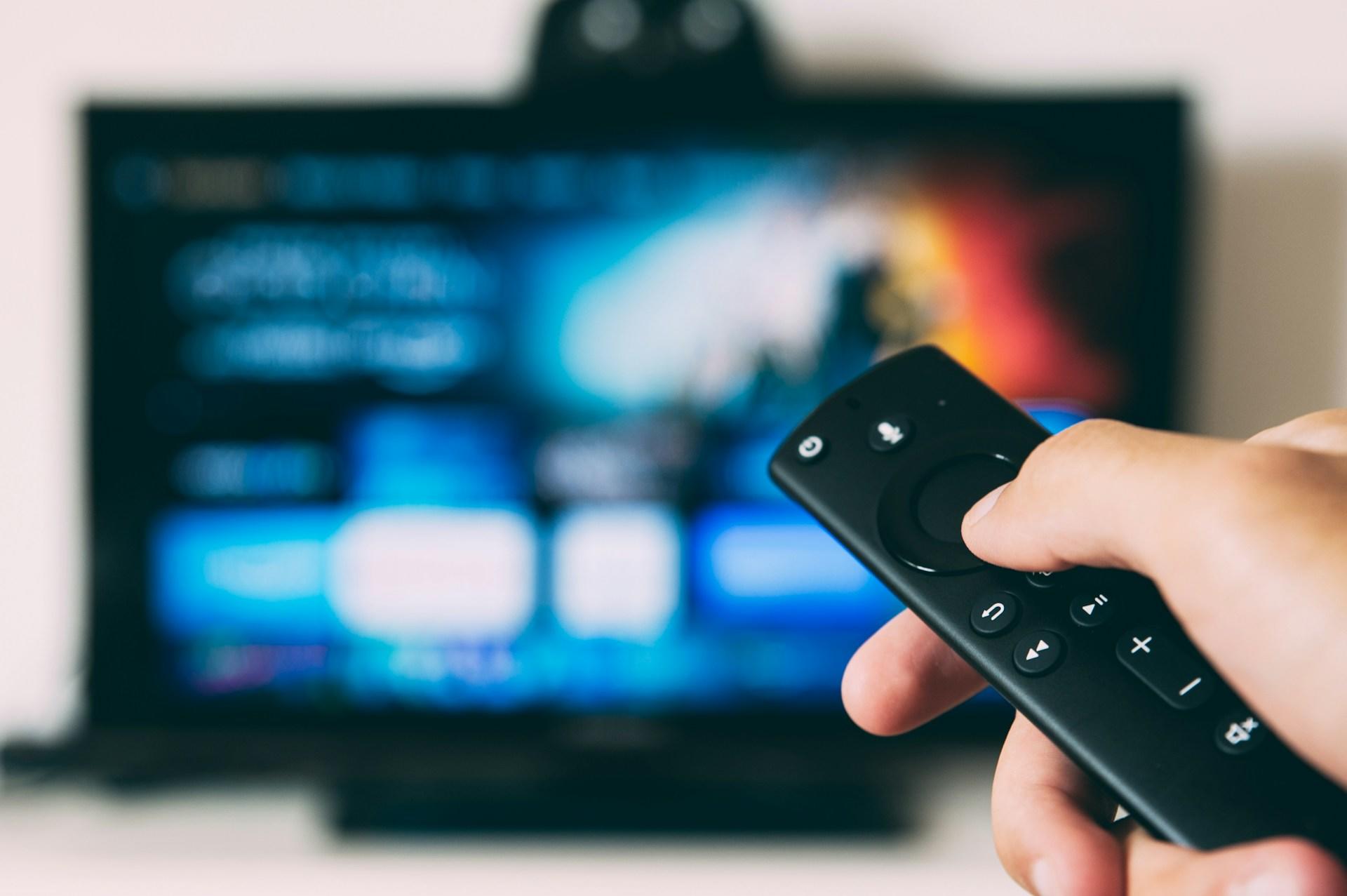 A person holding a remote control in front of a television screen.