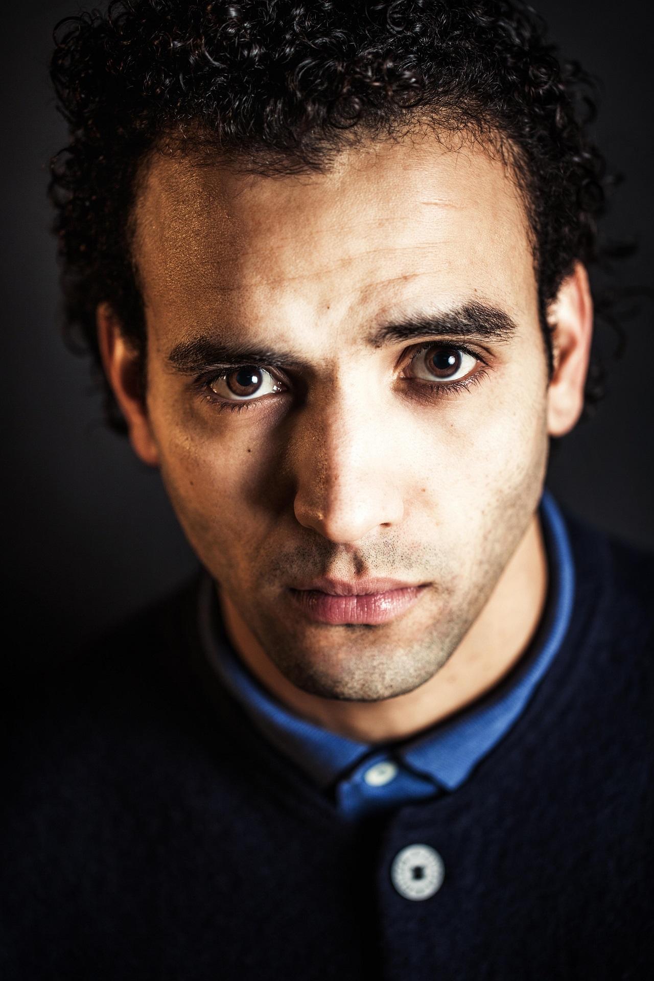 A closerup of a man wearing a blue shirt under a black jacket. 