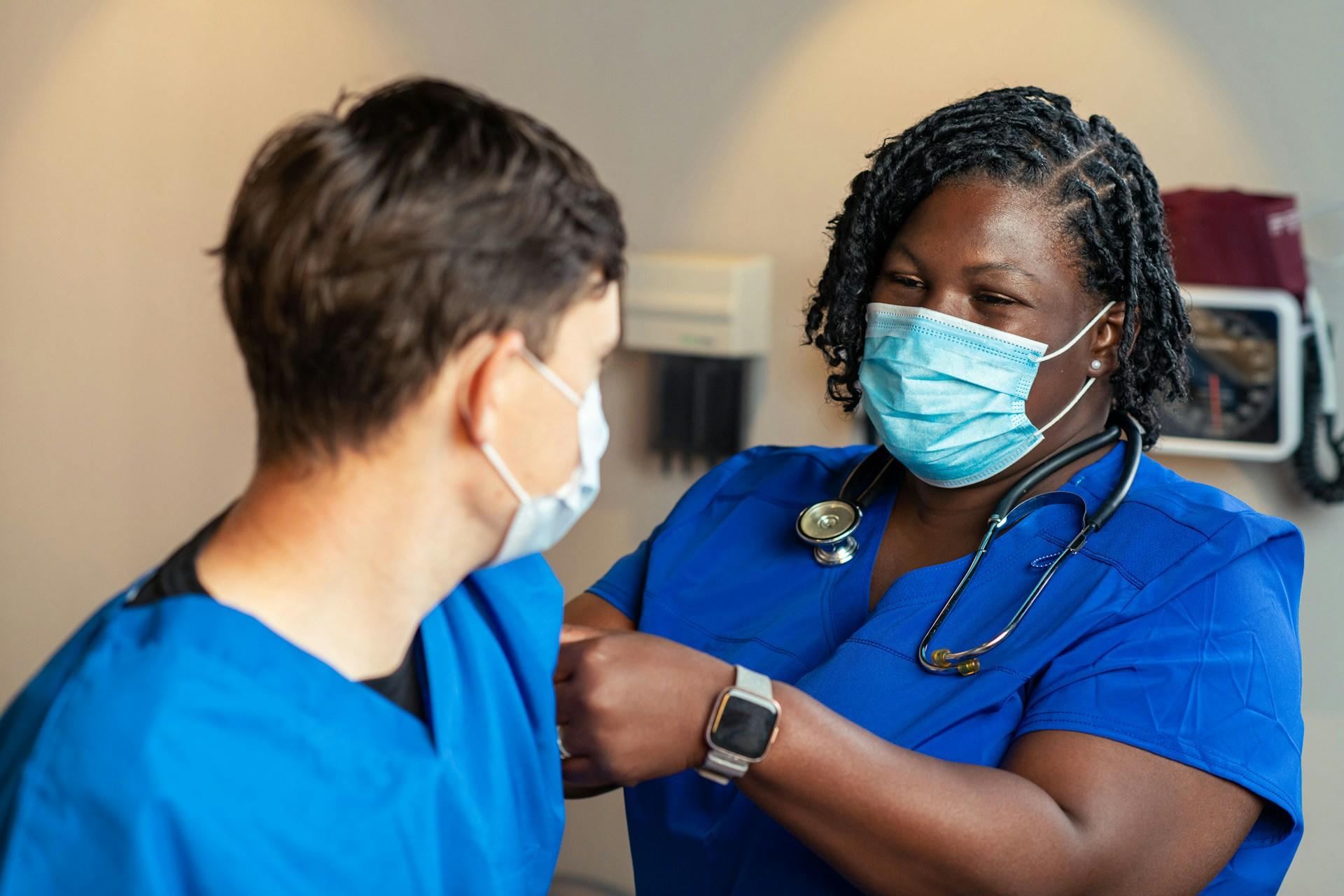 A nurse wearing a mask smiles and attends to a patient