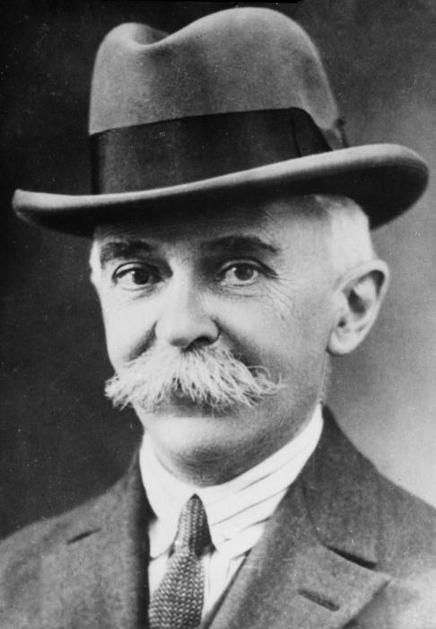 A black and white photo of Pierre de Coubertin with a moustache and a hat,.