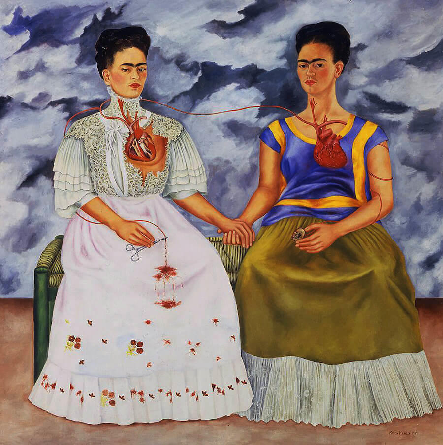 Two women sitting next to each other, holding hands, with a cloudy sky in the background.