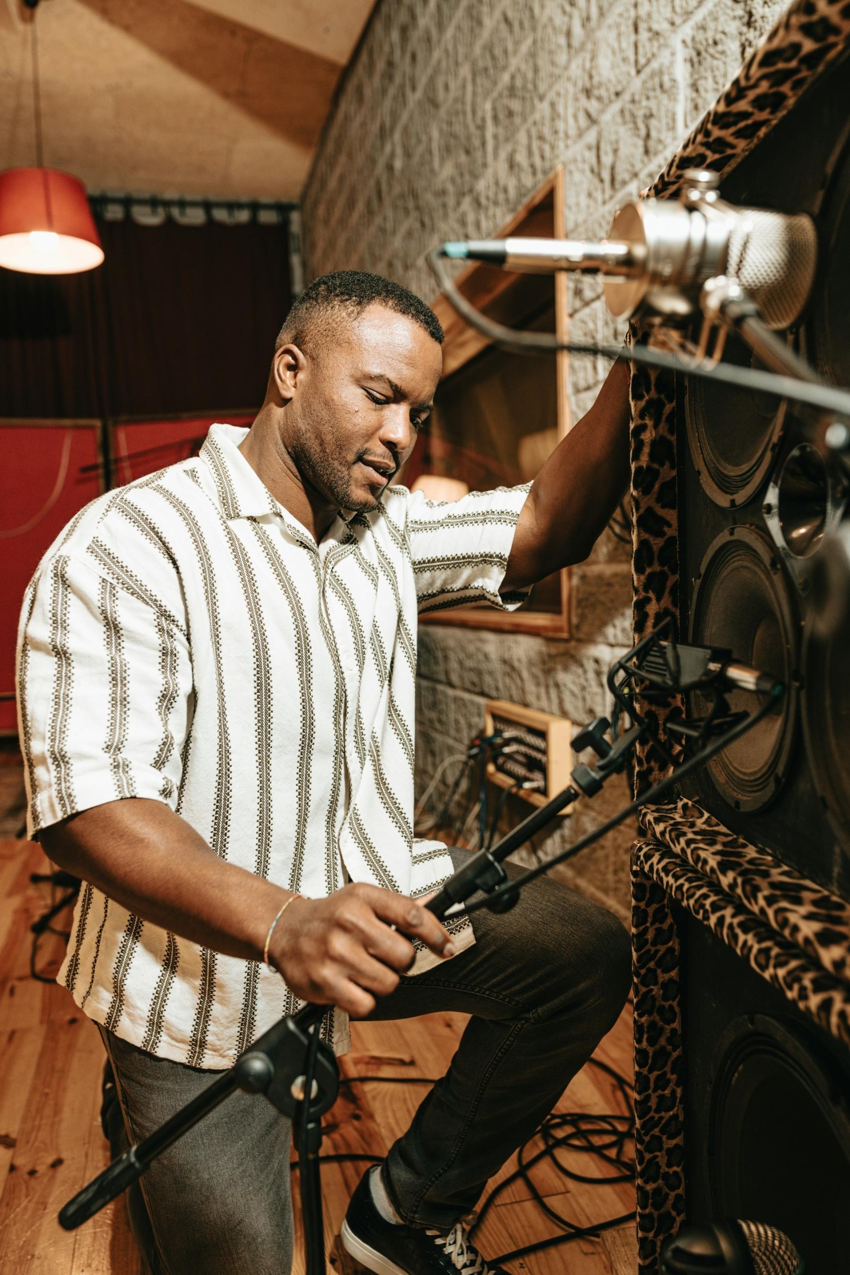 A man sets a microphone stand in front of a tall speaker stack. 