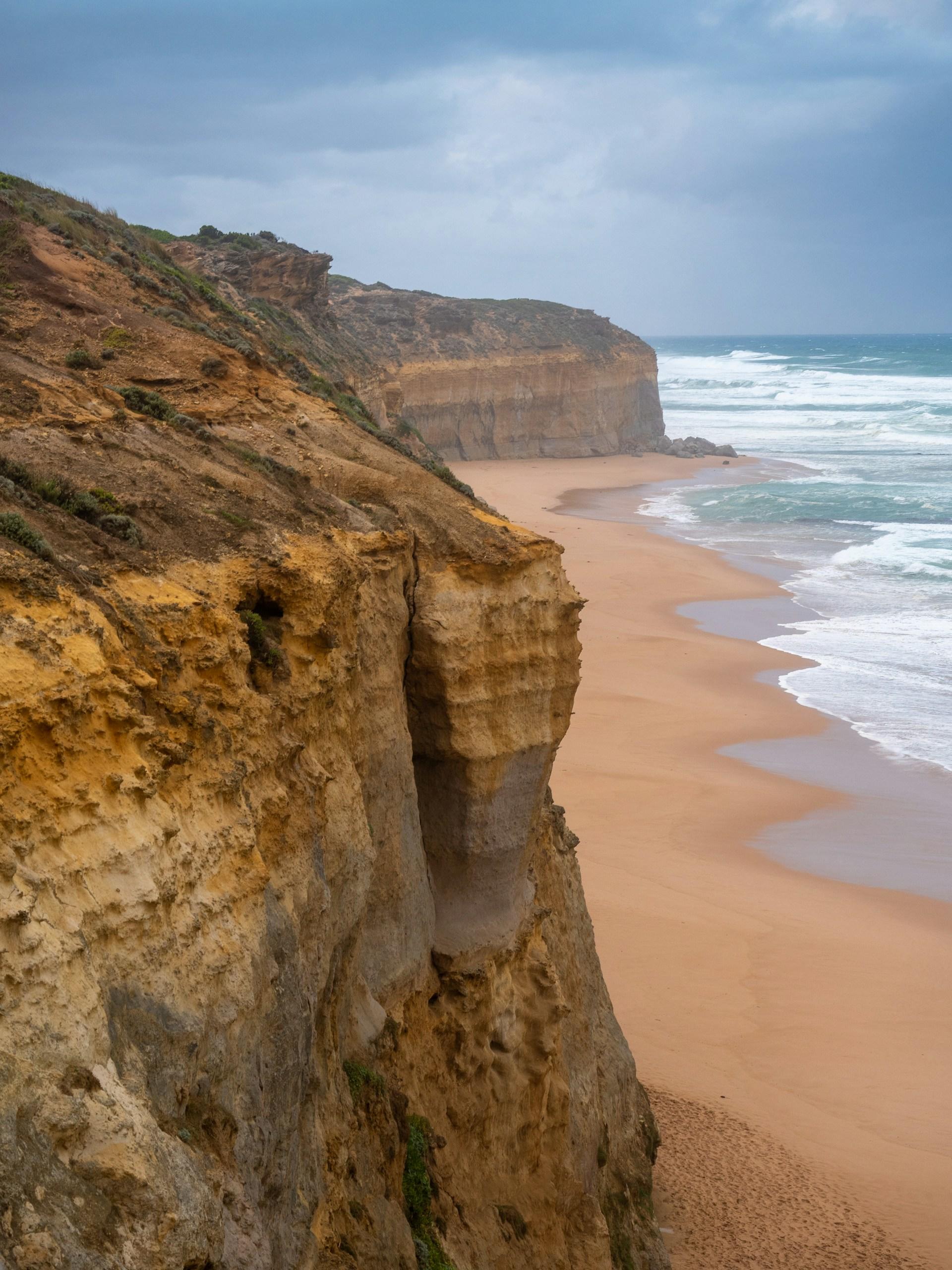 Brown cliffs and a beach on a cloudy day.