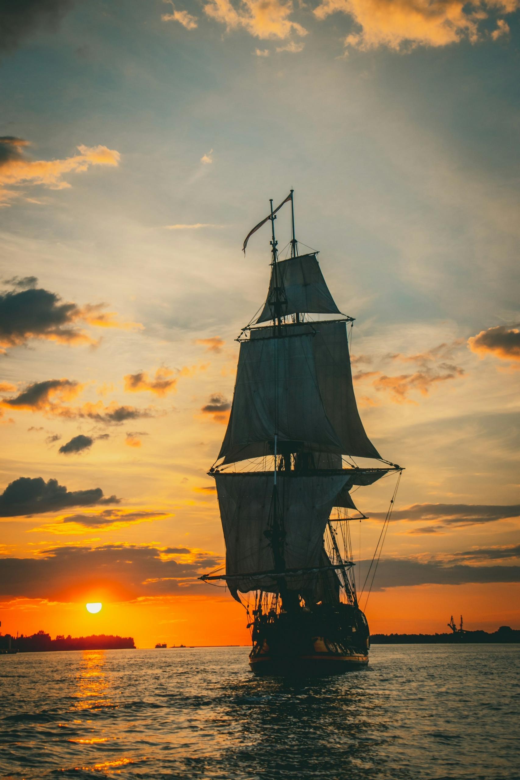 A tall-masted ship with sails unfurled at sunset.