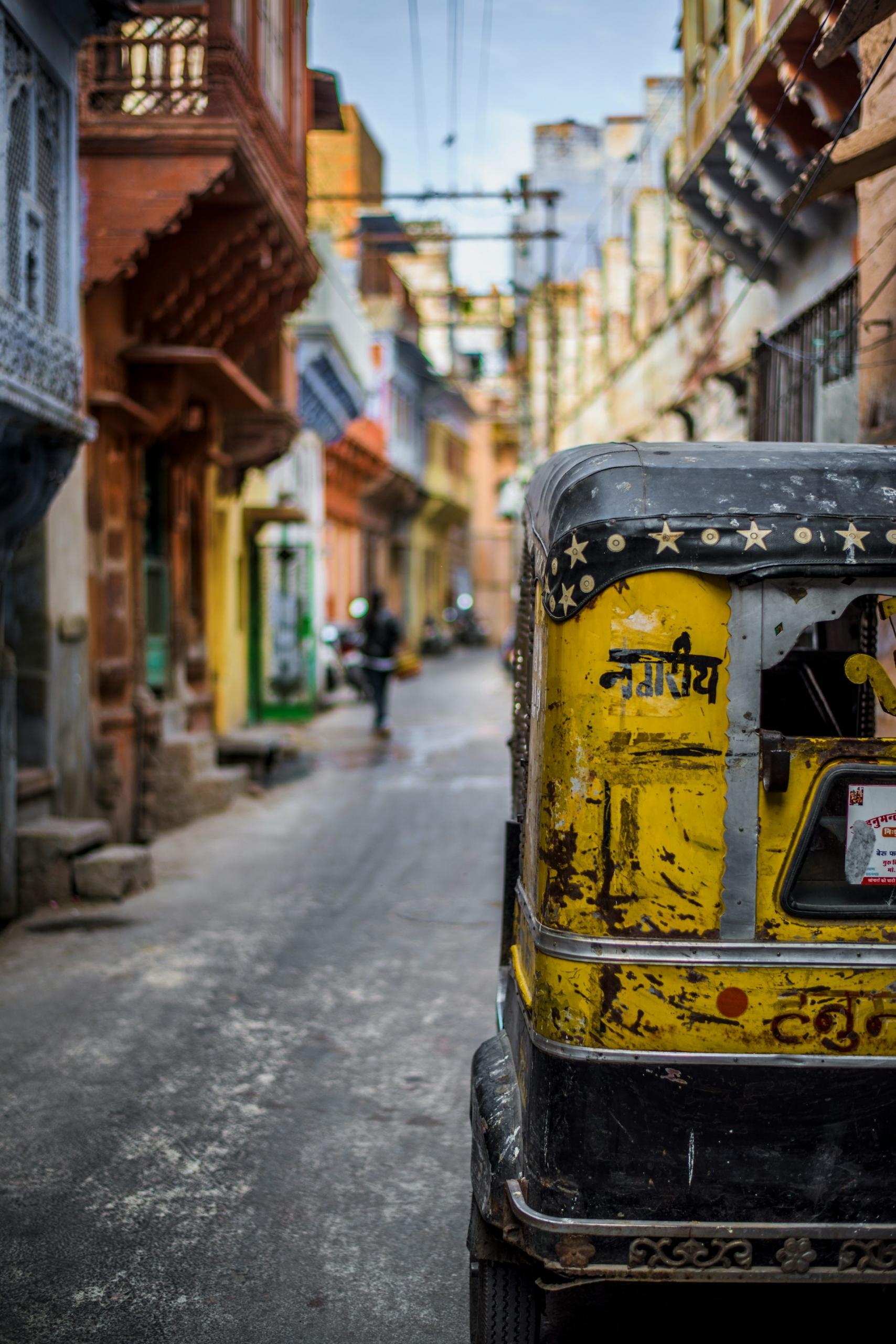 A narrow road with tall buildings on either side and a yellow scooter on it. 