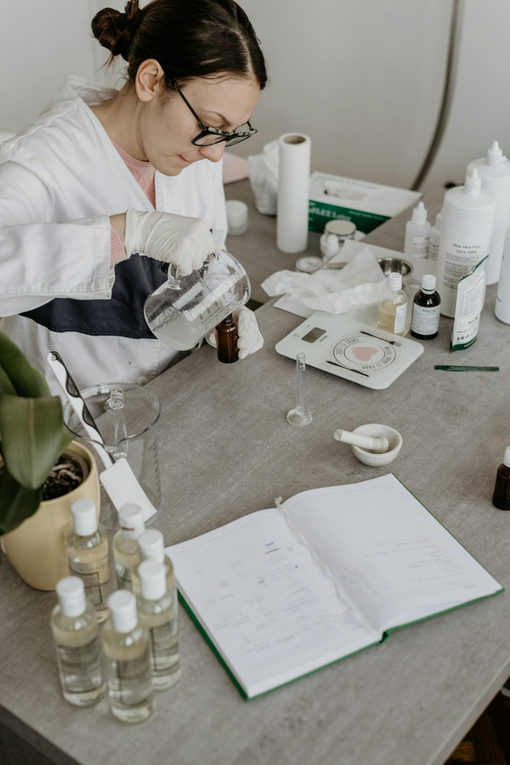 A person wearing a white coat and glasses sits at a lab bench.