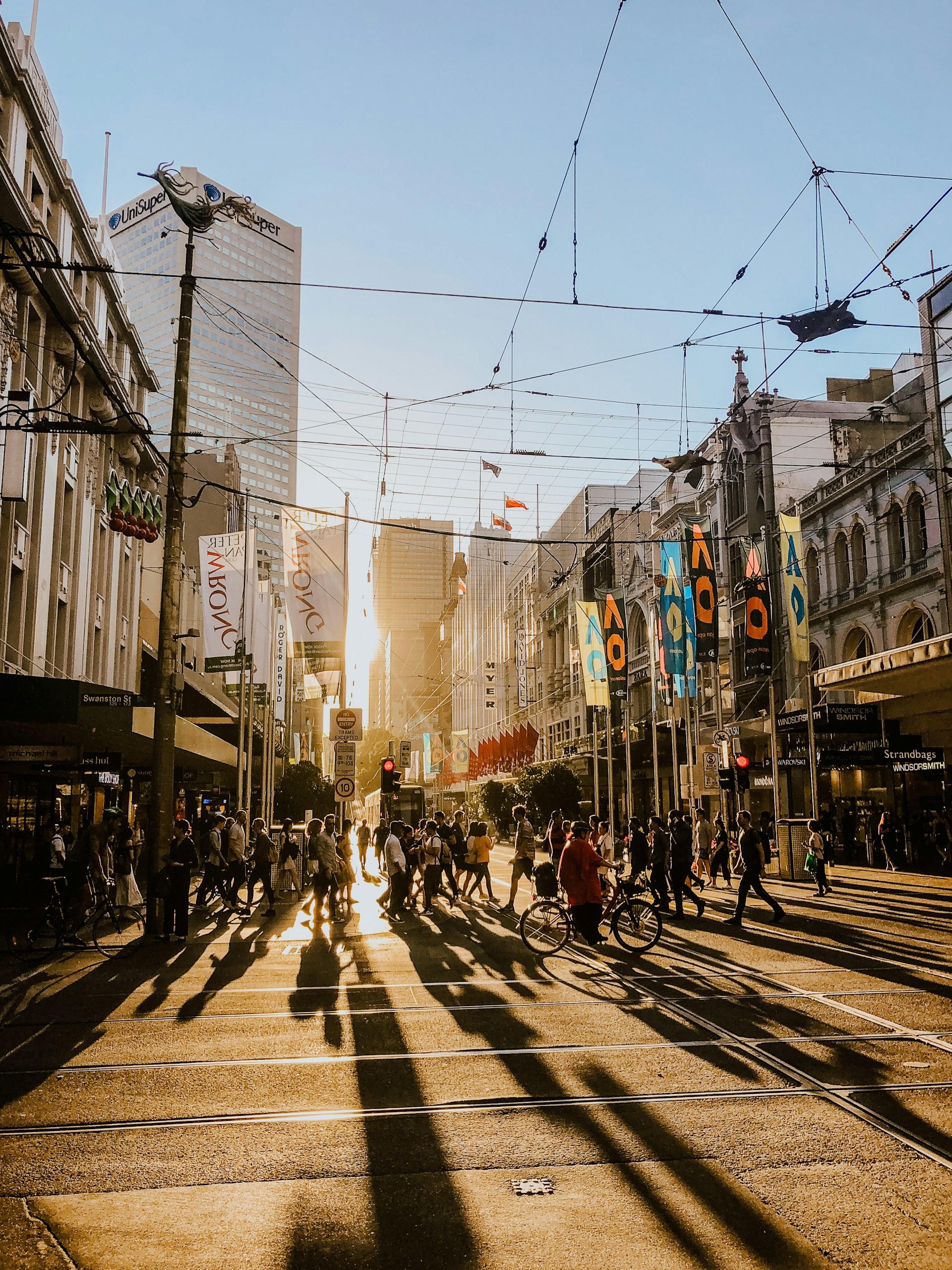 The rising sun shining on tram tracks with people milling about.