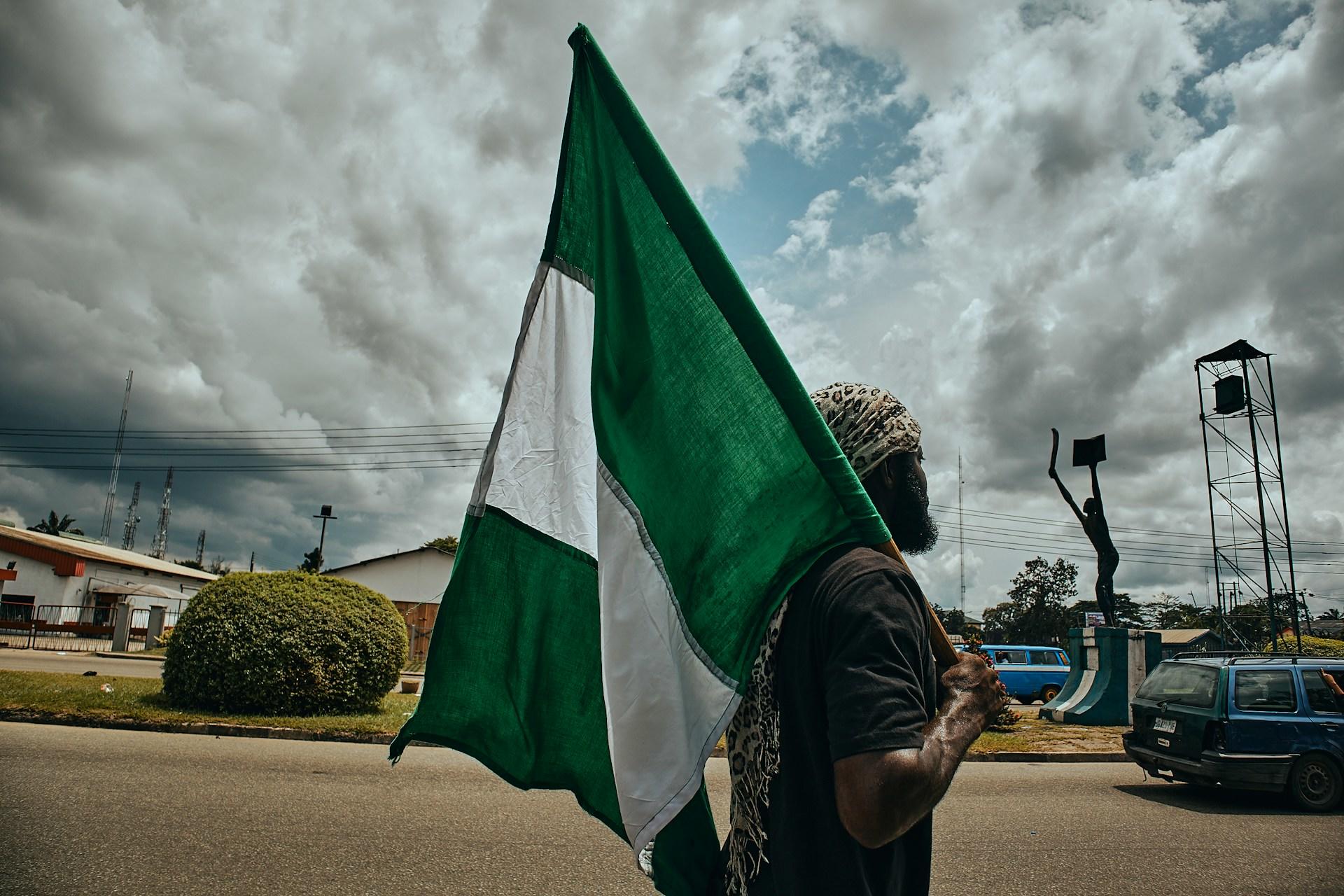 A man holds the Nigerian flag on a street on a cloudy day.