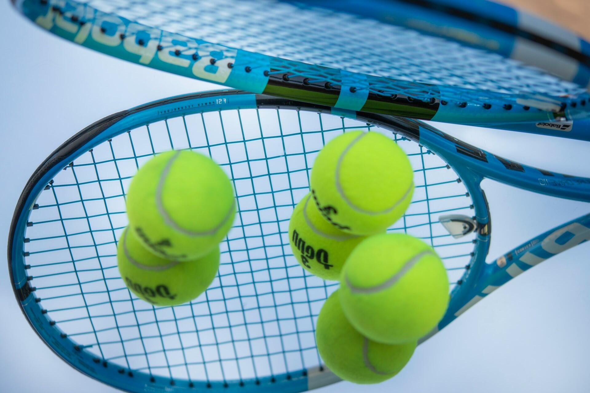 Close-up of blue tennis rackets with yellow tennis balls resting on the strings.