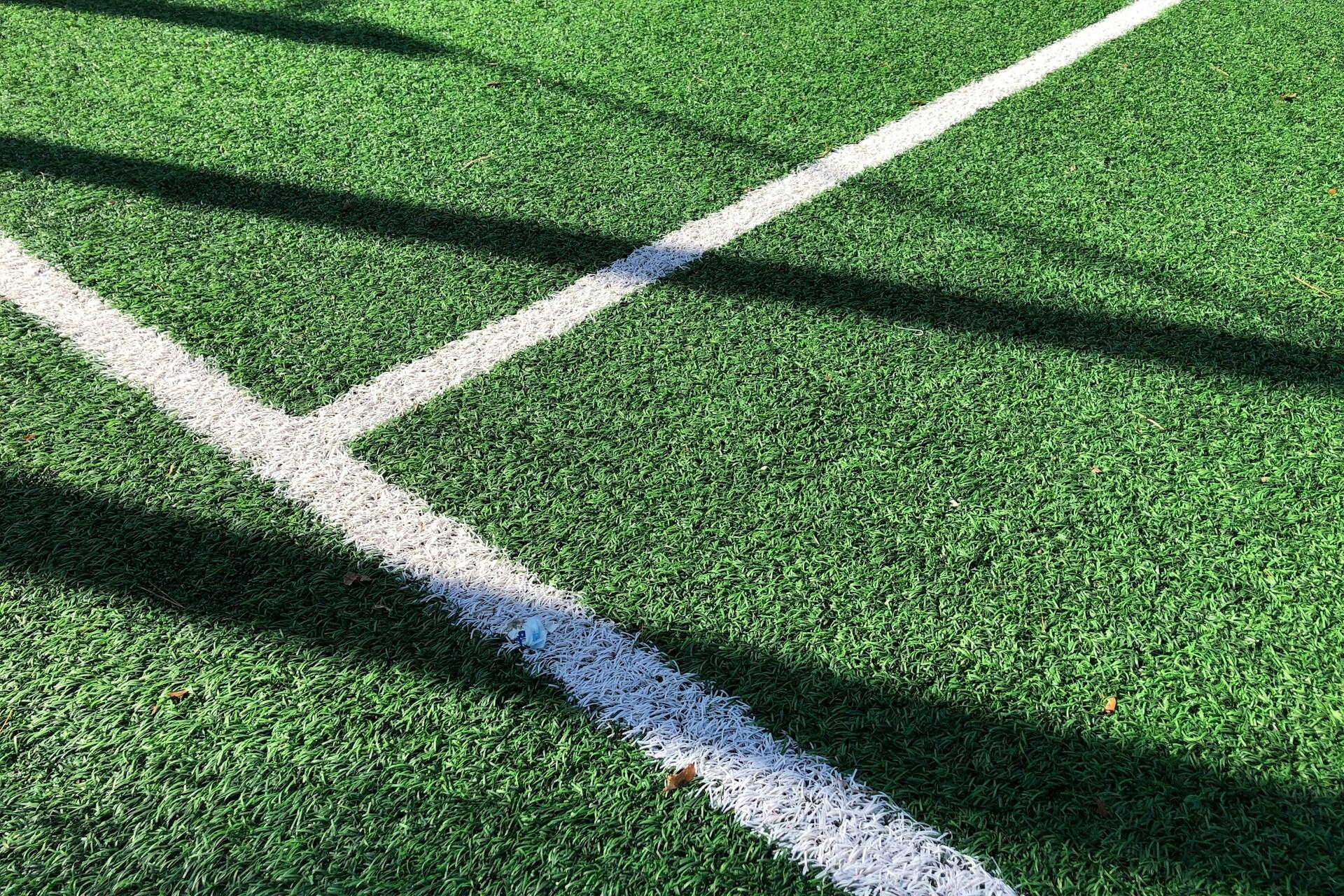 A close-up of white tennis court lines on green turf with shadows crossing the surface.