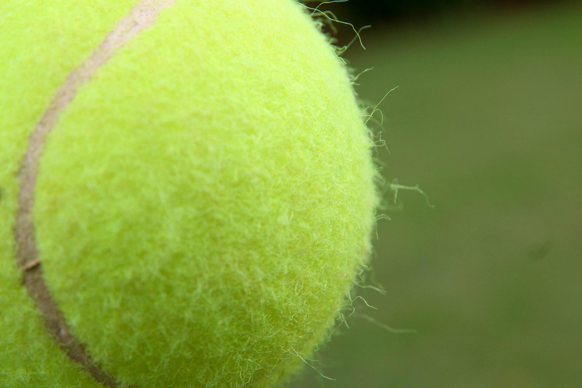 A close-up of a yellow tennis ball against a blurred green background.