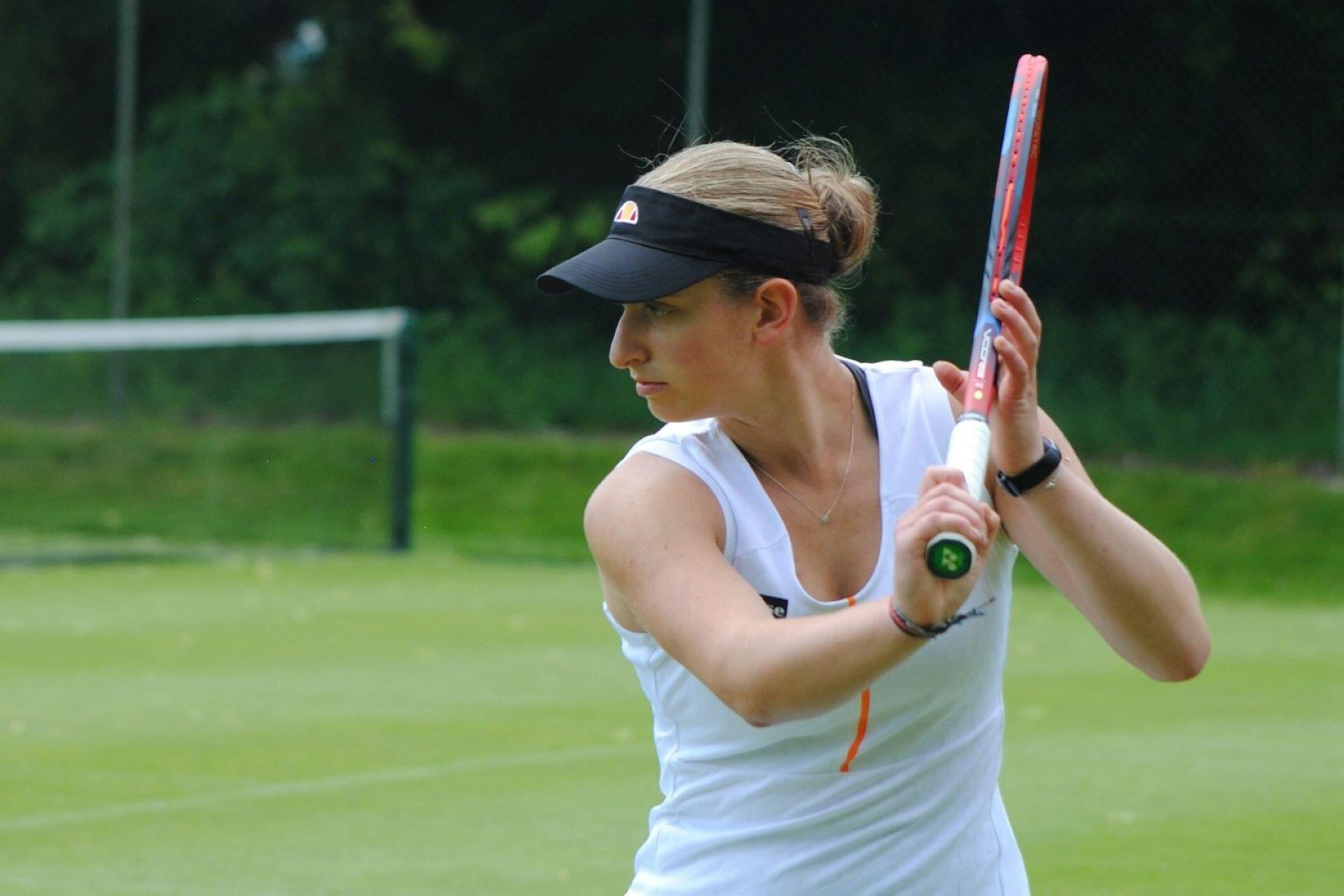 Woman holding a tennis racket on a grass court while preparing to return a shot.