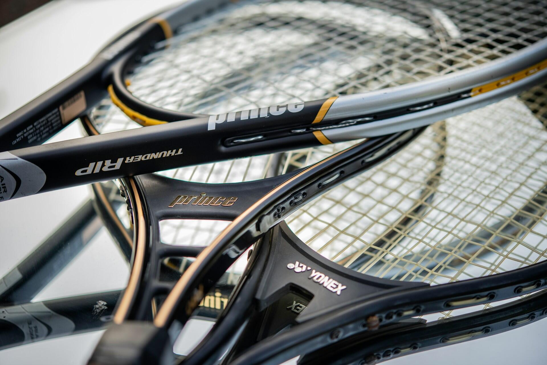 Close-up of several black Prince tennis rackets stacked together, with strings and frames visible.