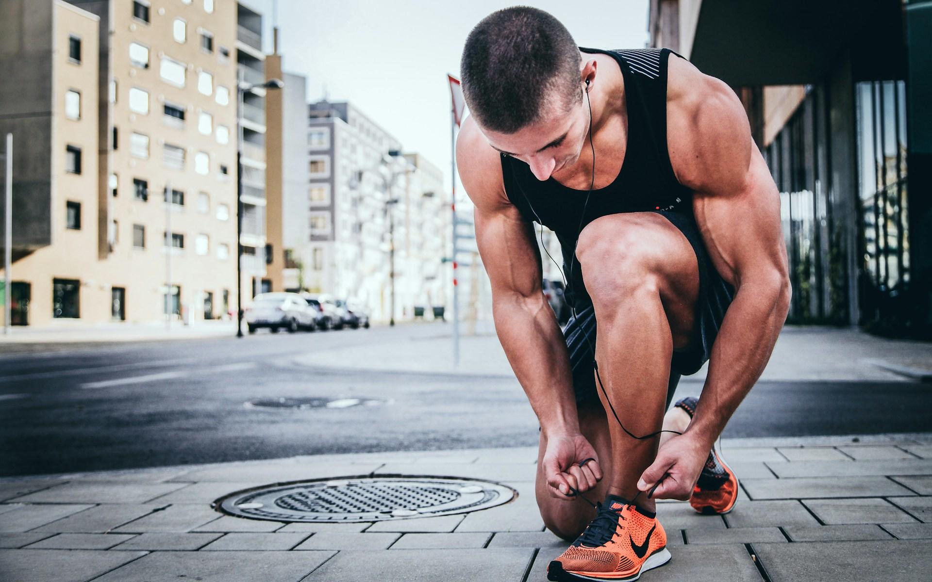 A person wering summer athletic wear ties their shoe on a street.