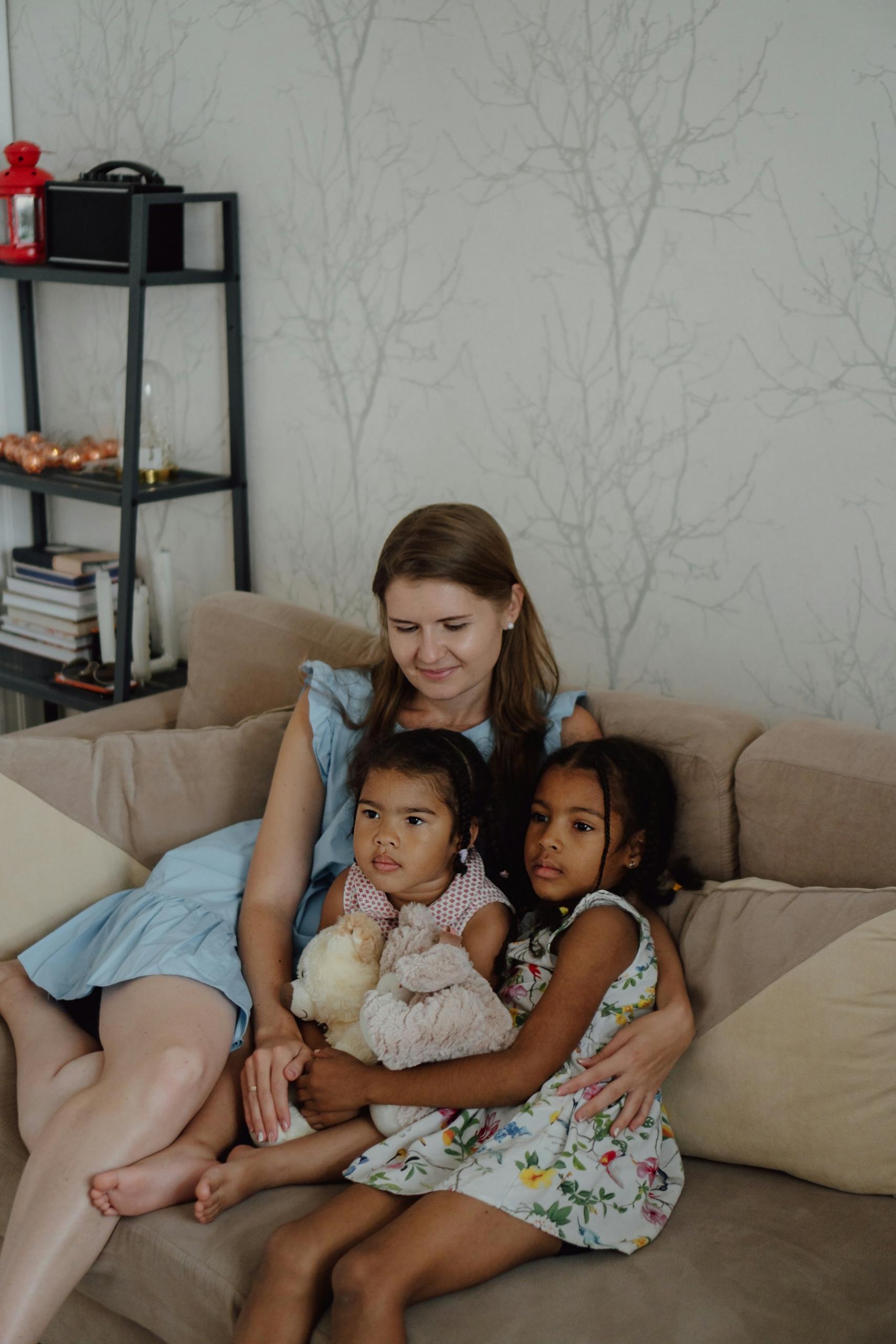 A woman sits with two small children on a couch.