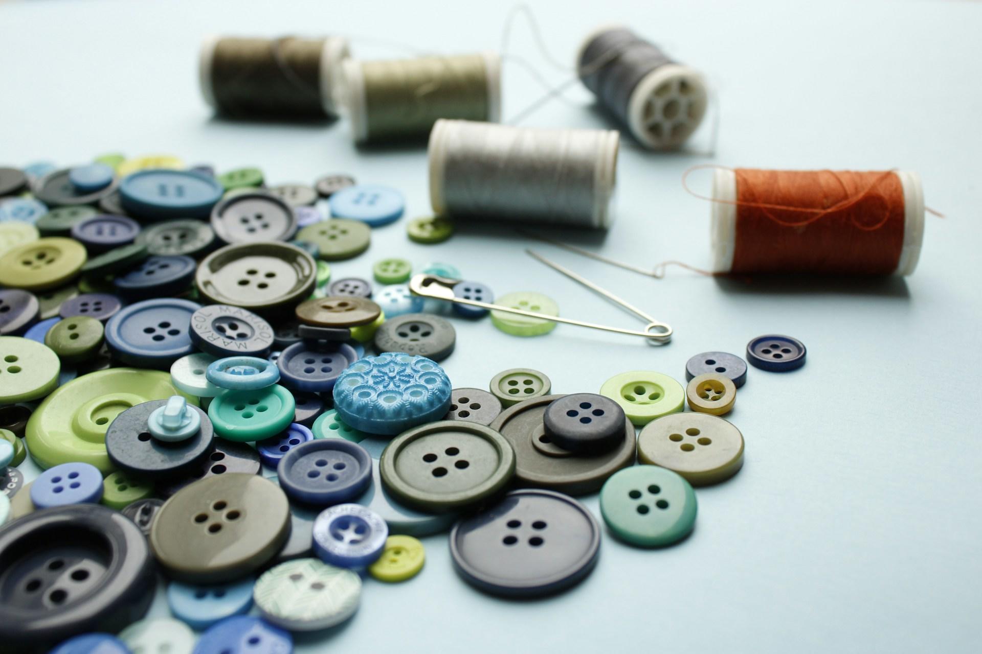 A pile of buttons next to some thread and some needles.
