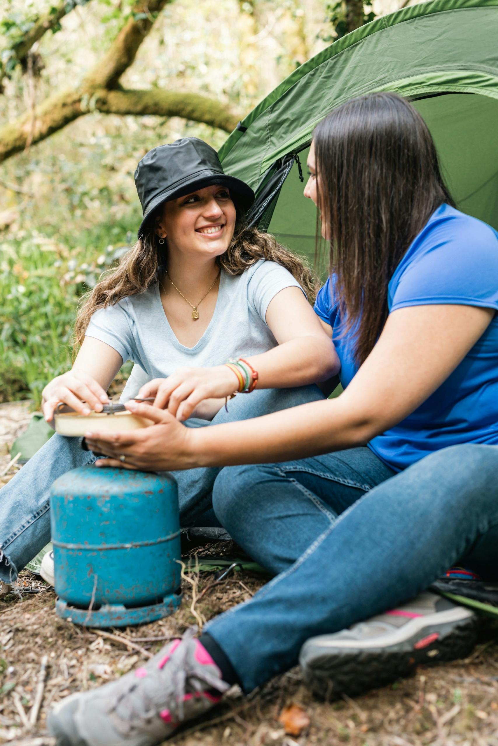 Two young women sit on the ground with a blue gas bottle in front of them.