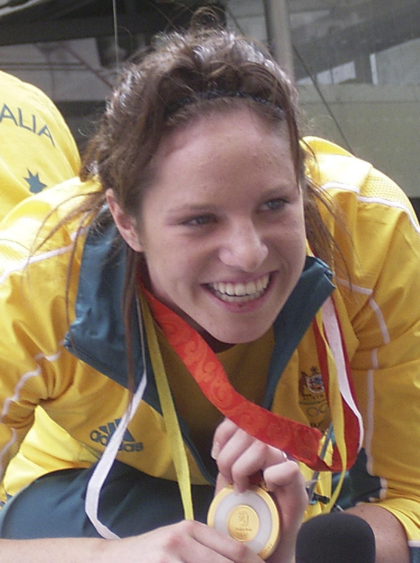 A woman wearing yellow and blue athletic gear shows her medal. 