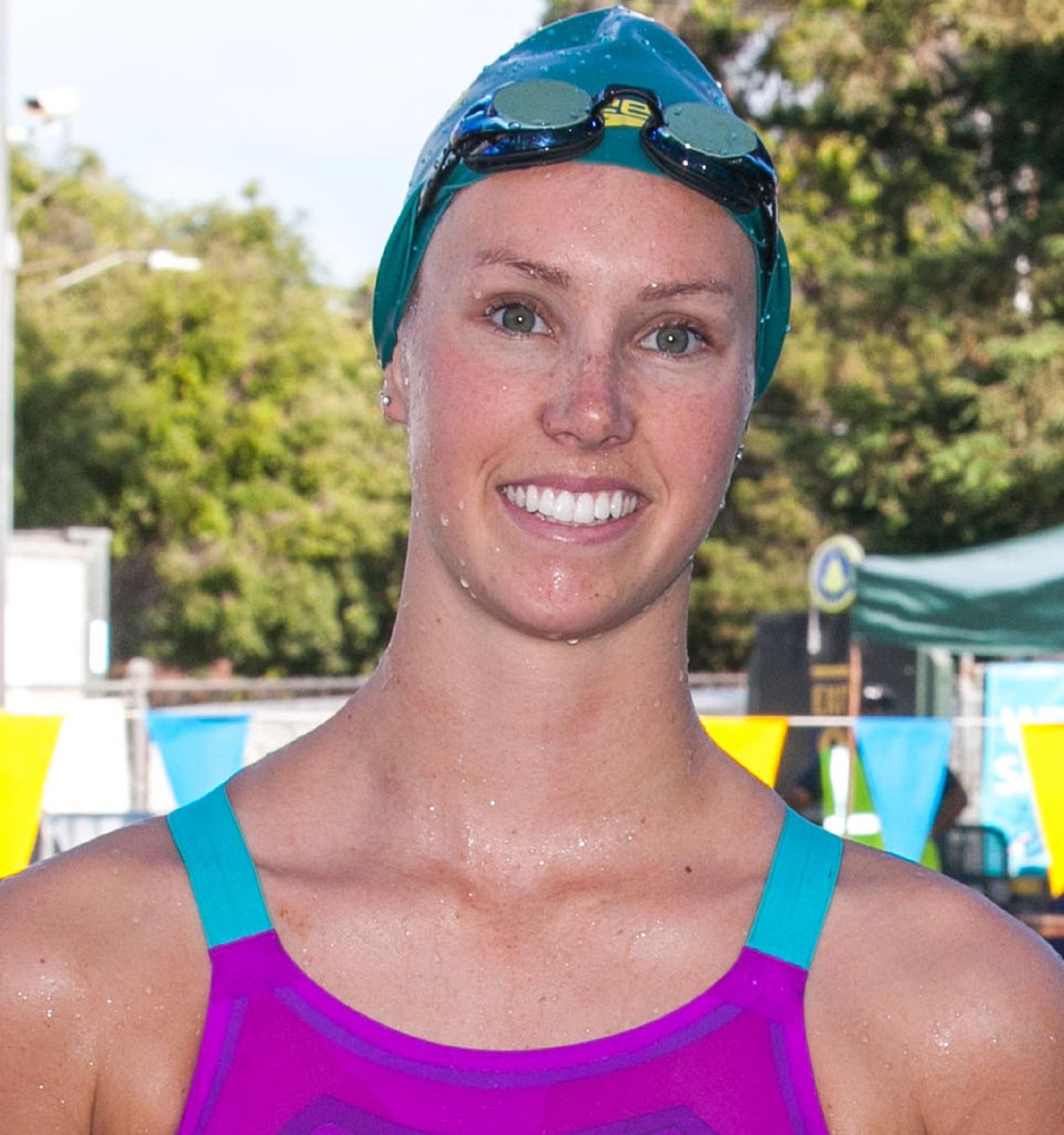 A woman wearing a swim cap and goggles outside on a sunny day. 