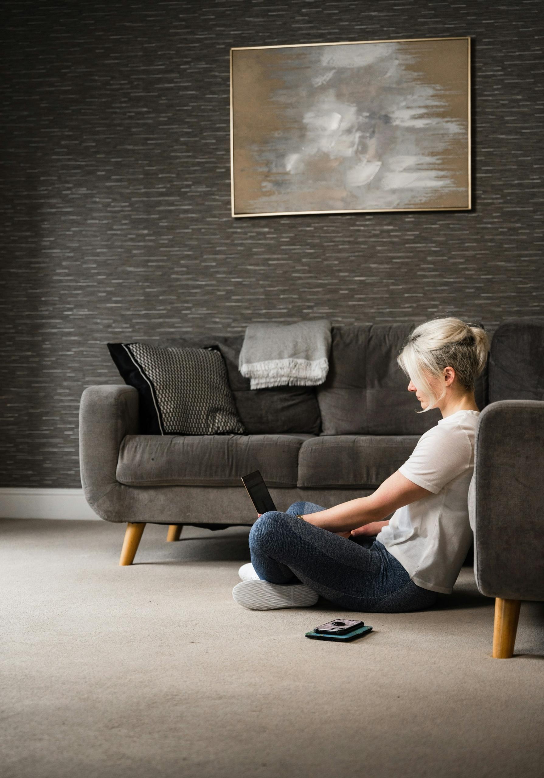 A blond woman sitting cross-legged on the floor with a computer in her lap.