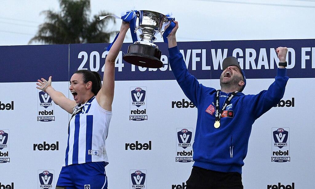 A woman and a man stand on a stage, raising a trophy together.