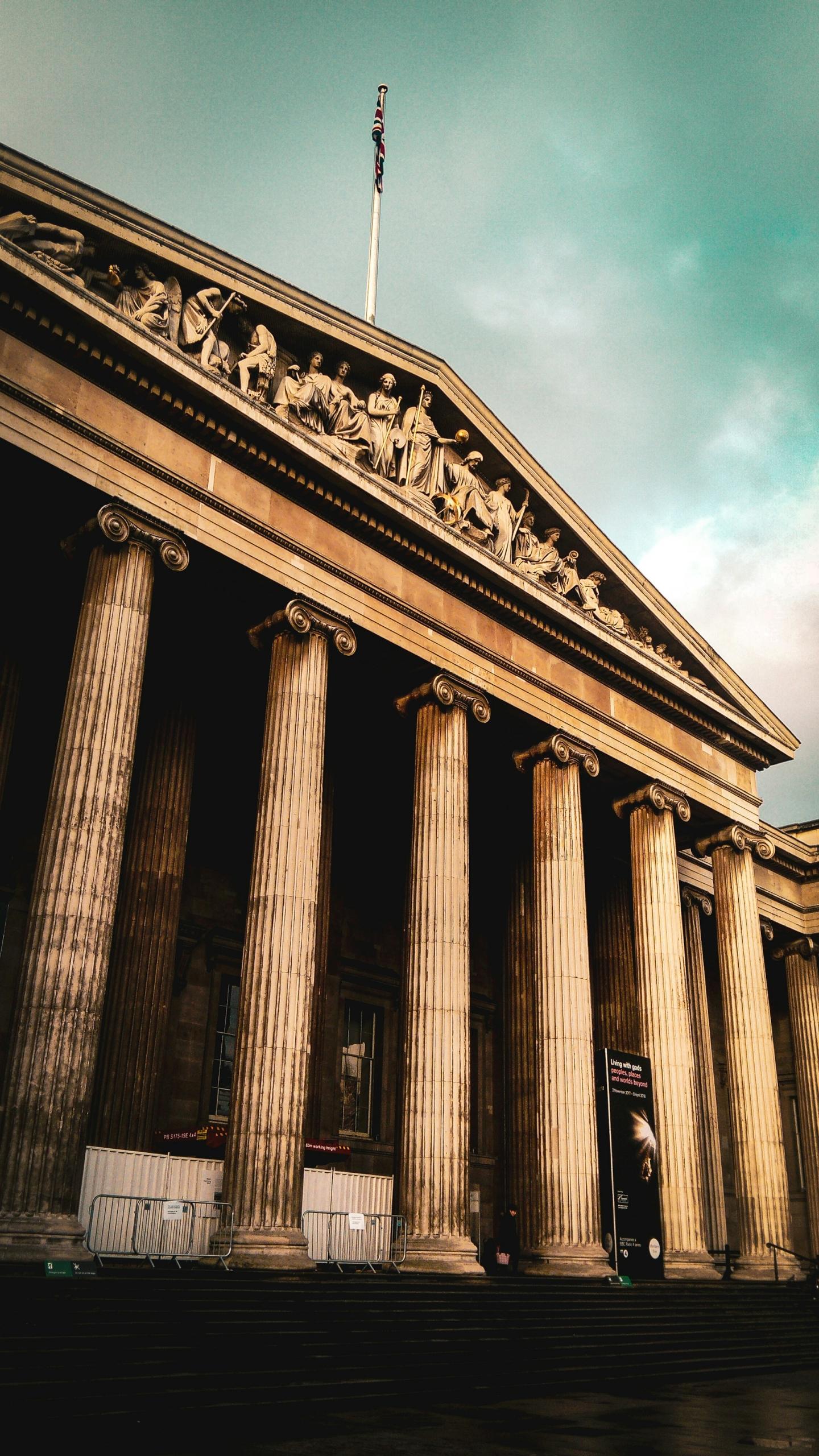 A stone building with columns and a frieze over the entryway on a cloudy day. 