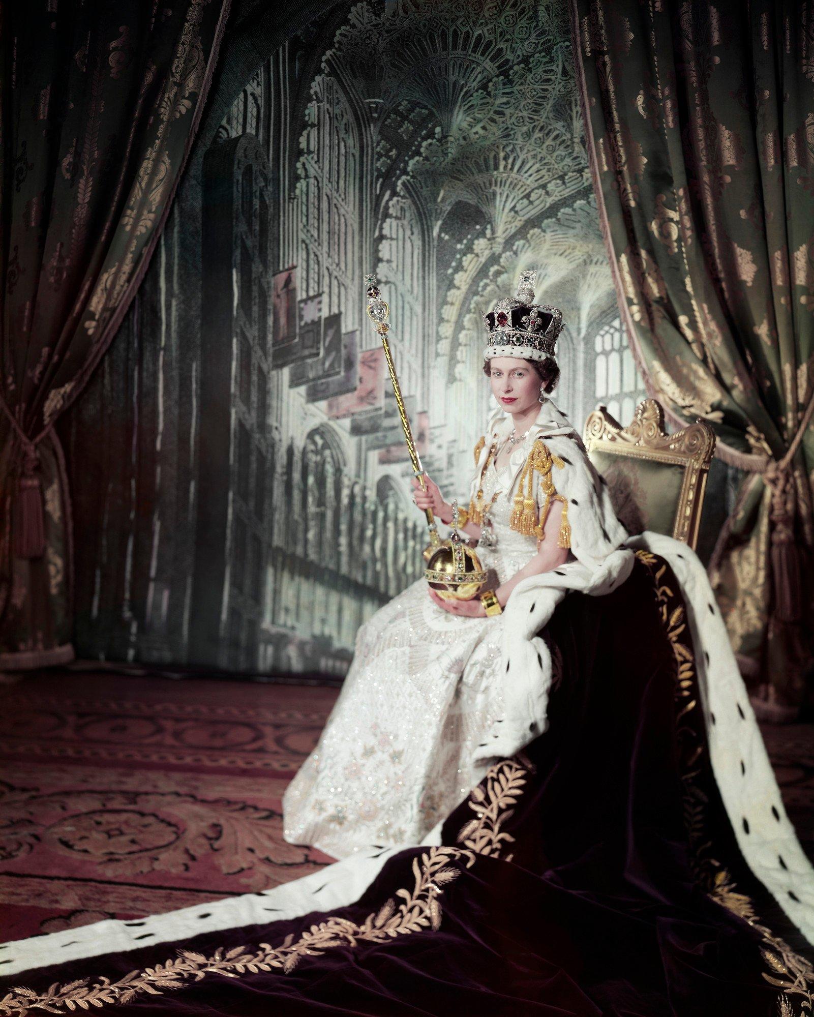 The Queen sits, wearing ermine and holding coronation regalia. 