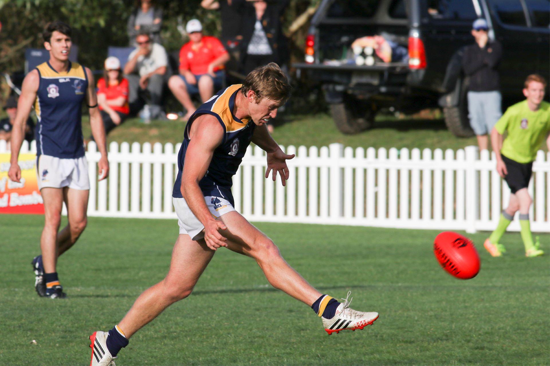 An Aussie rules player kicking the ball.