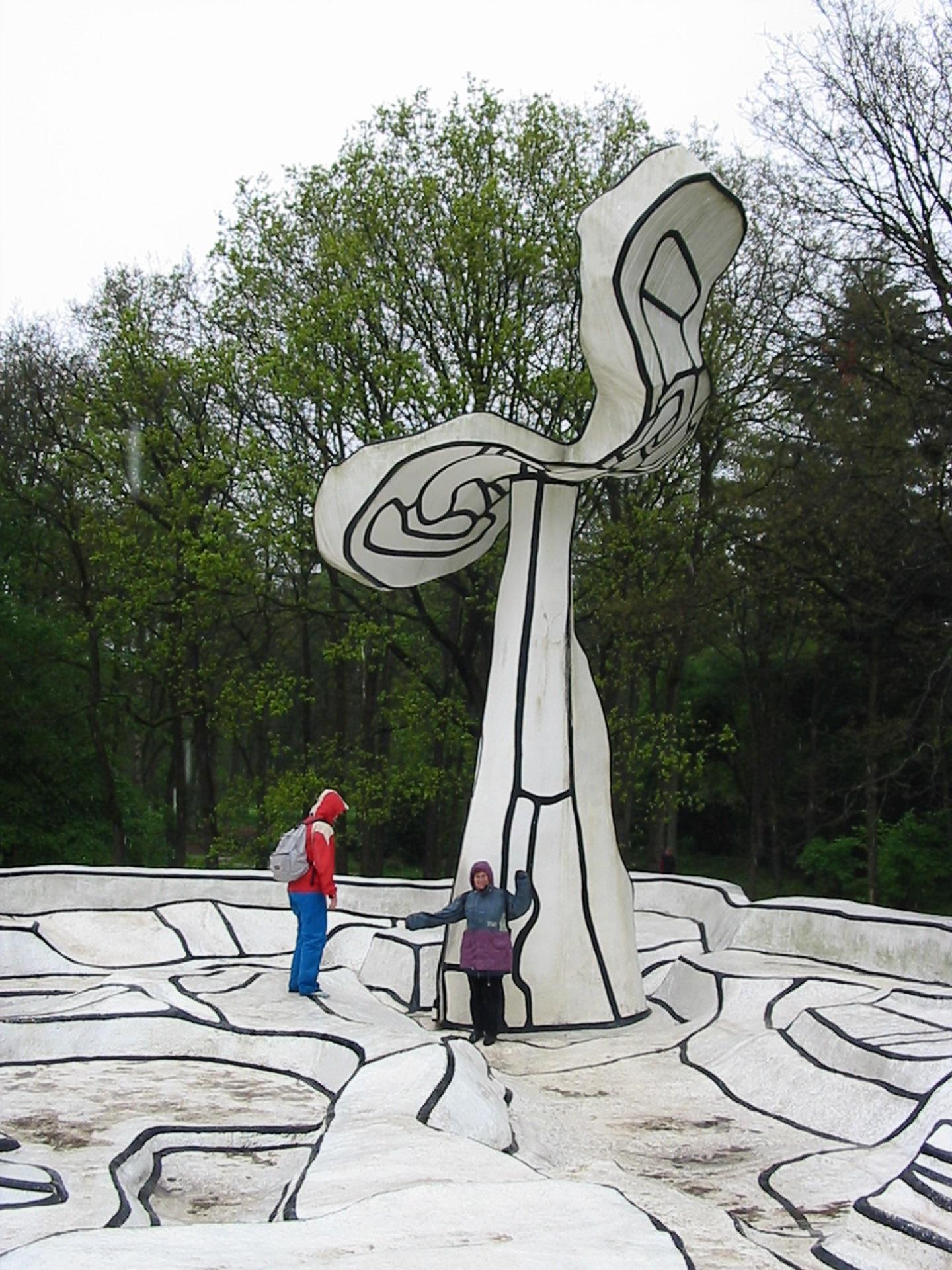 A black and white sculpture with trees behind it. 
