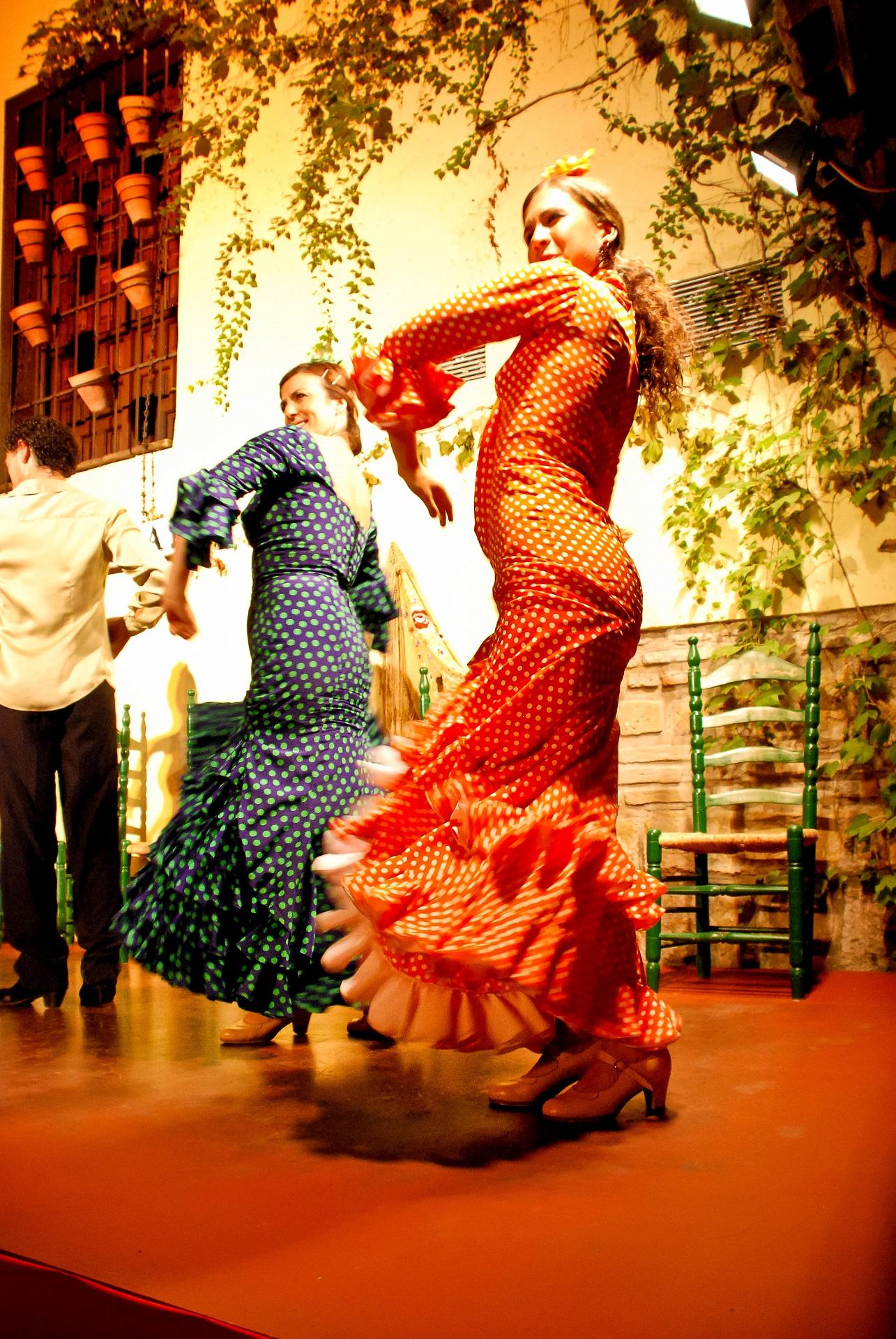 Two women wearing long dresses dance onstage. 