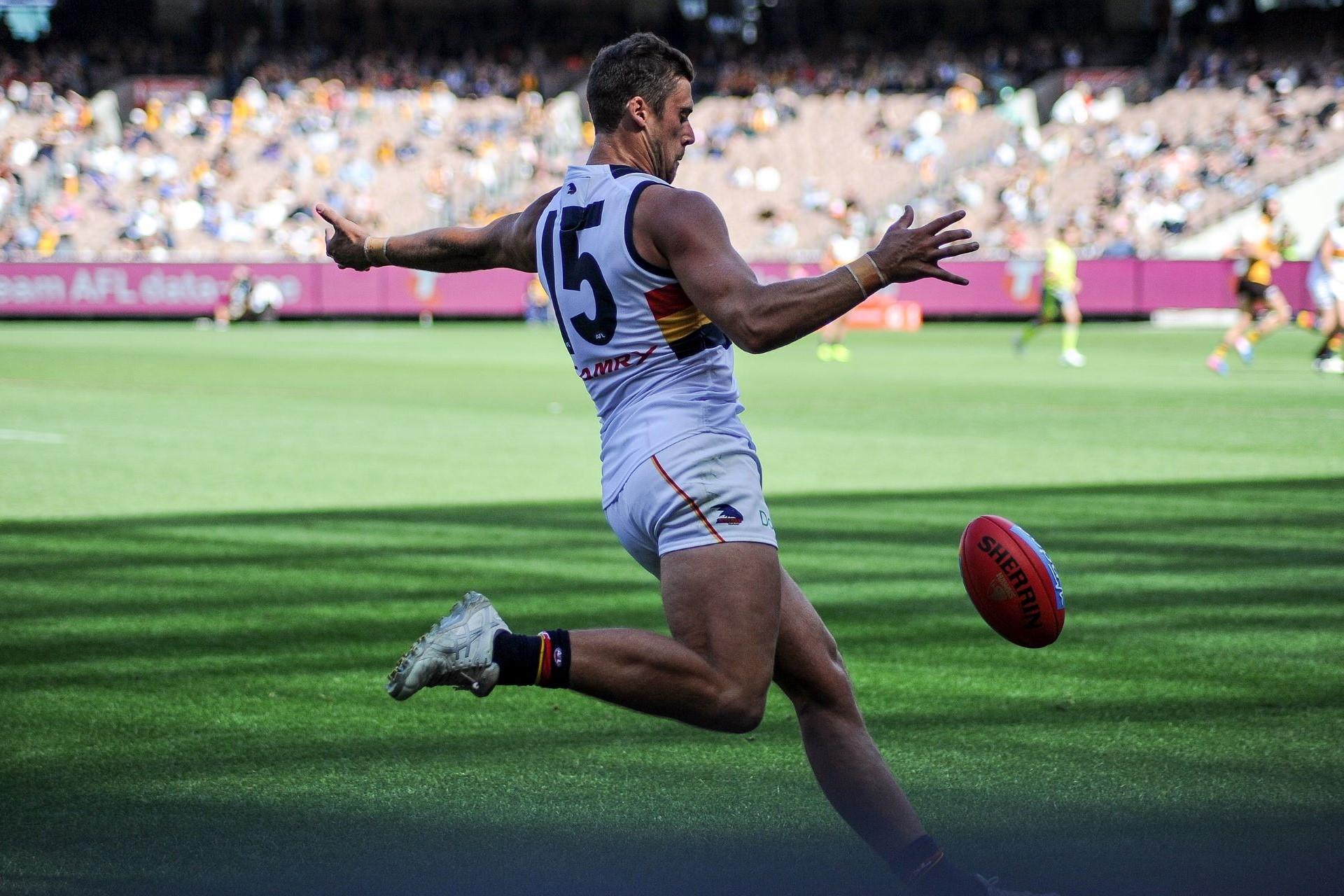 An Aussie Rules player kicking the ball.