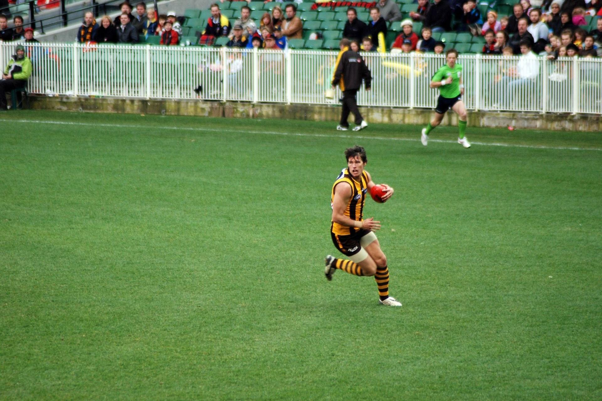 An Aussie rules player running with the ball.