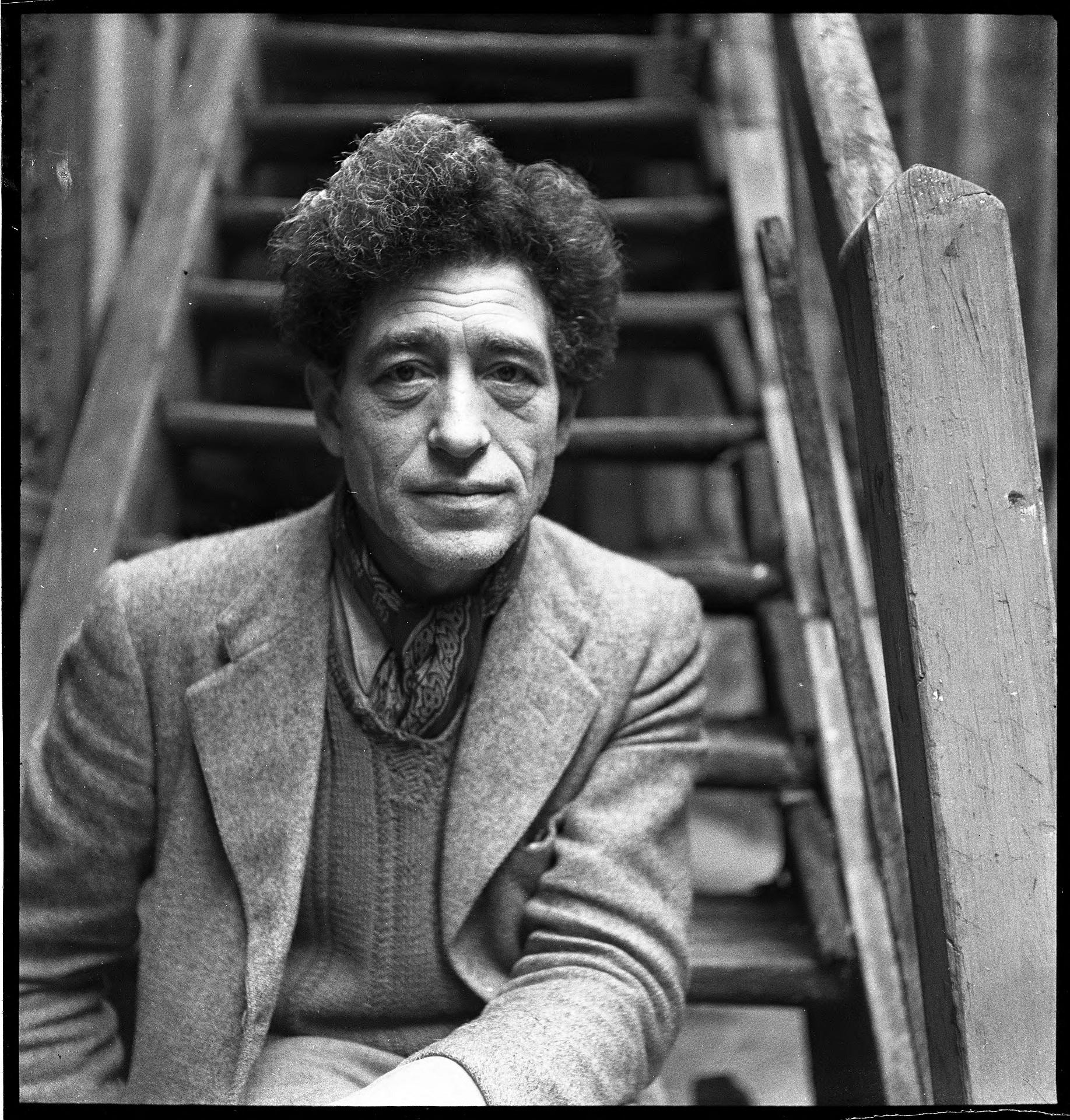 A greyscale of a man wearing a suit jacket, sitting on outdoor stairs.