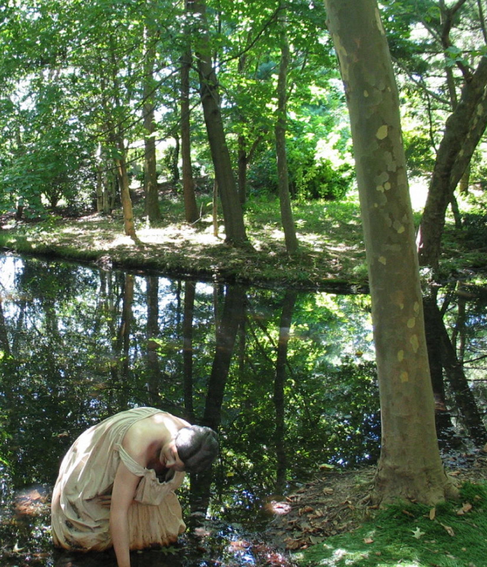 A sculpture installed in a wooded area next to a small pond. 