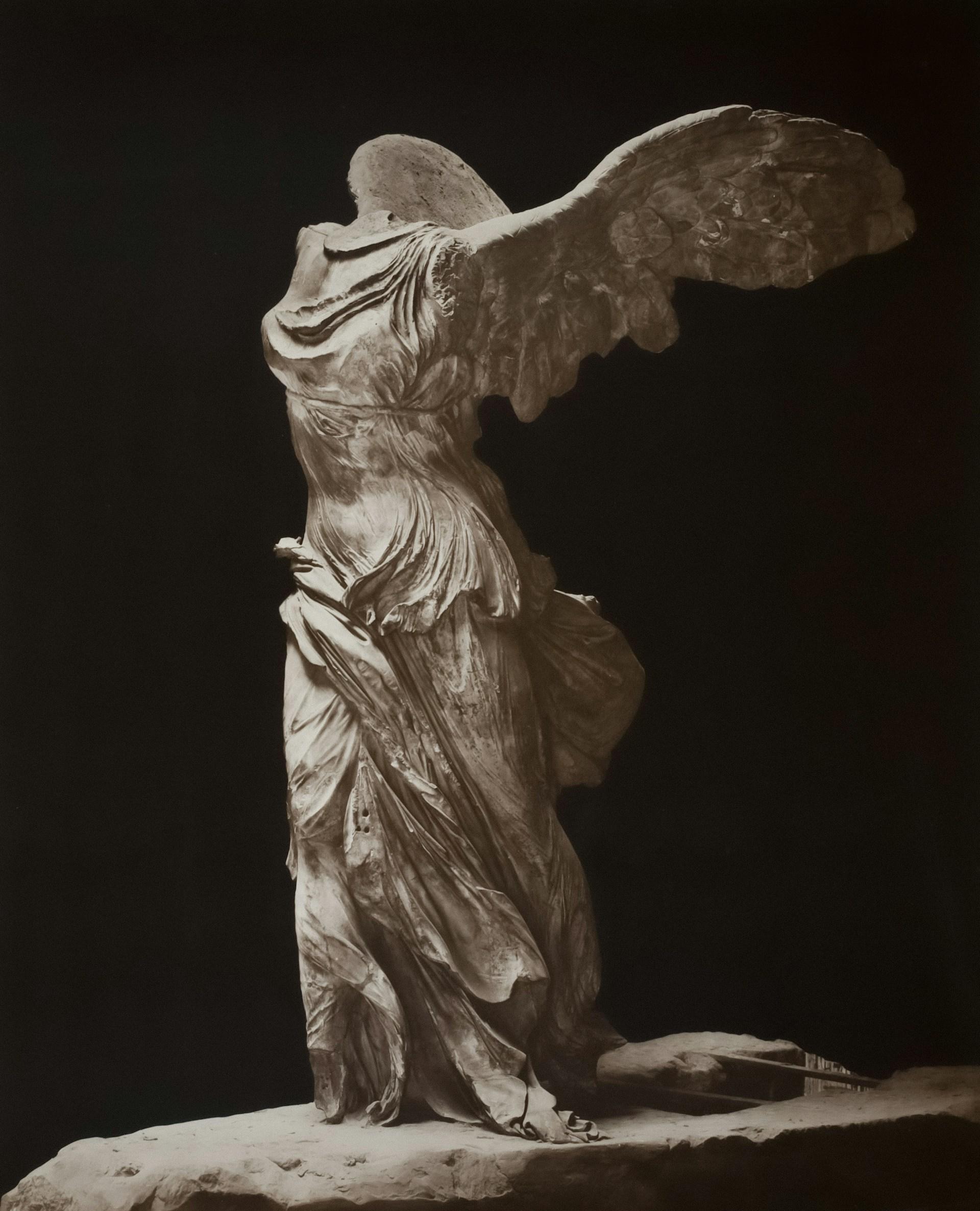 A winged statue missing its head, against a black background. 