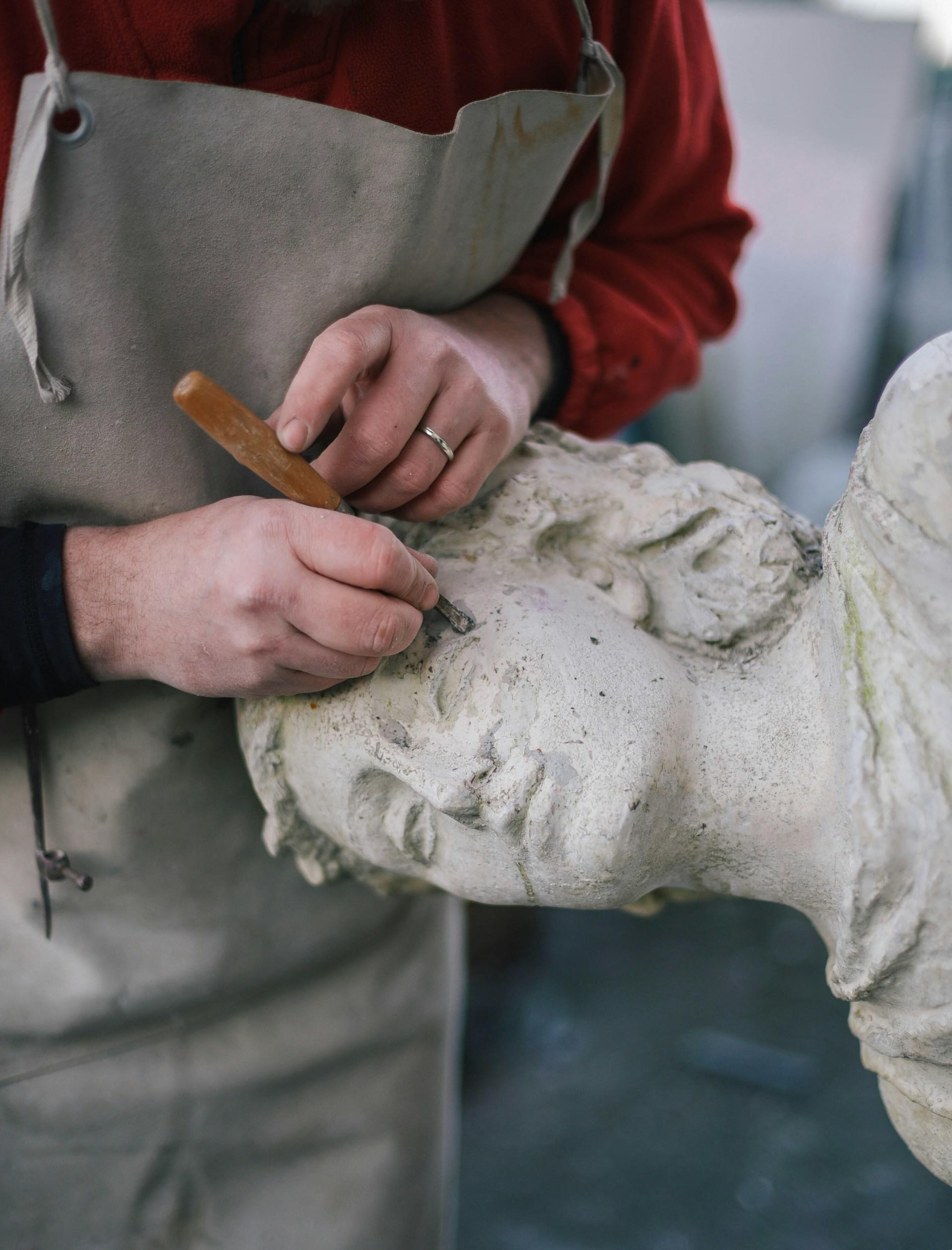 A person sculpts lines in a stone figure's face. 