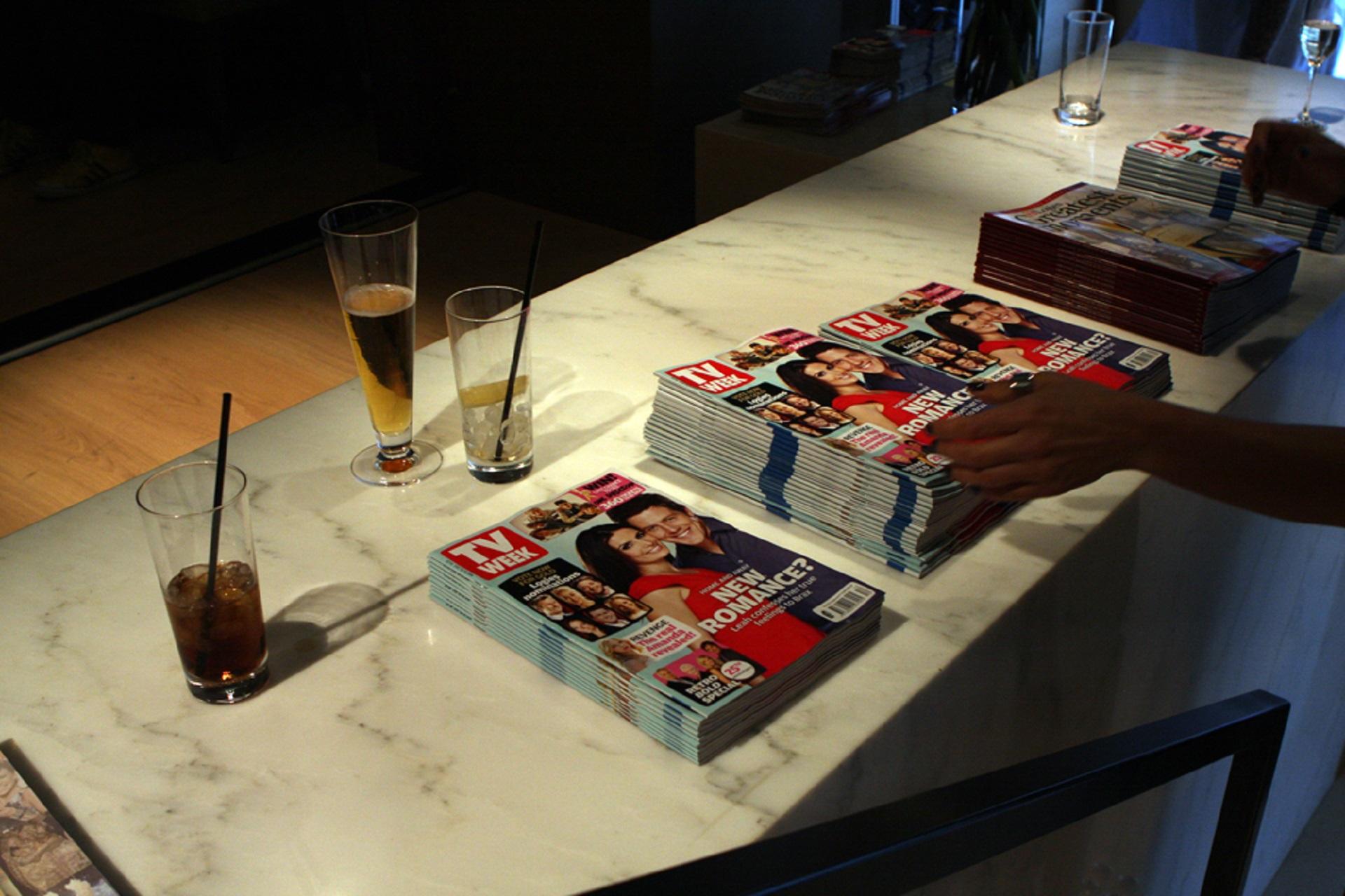 A stack of magazines on a white table with three drink glasses.