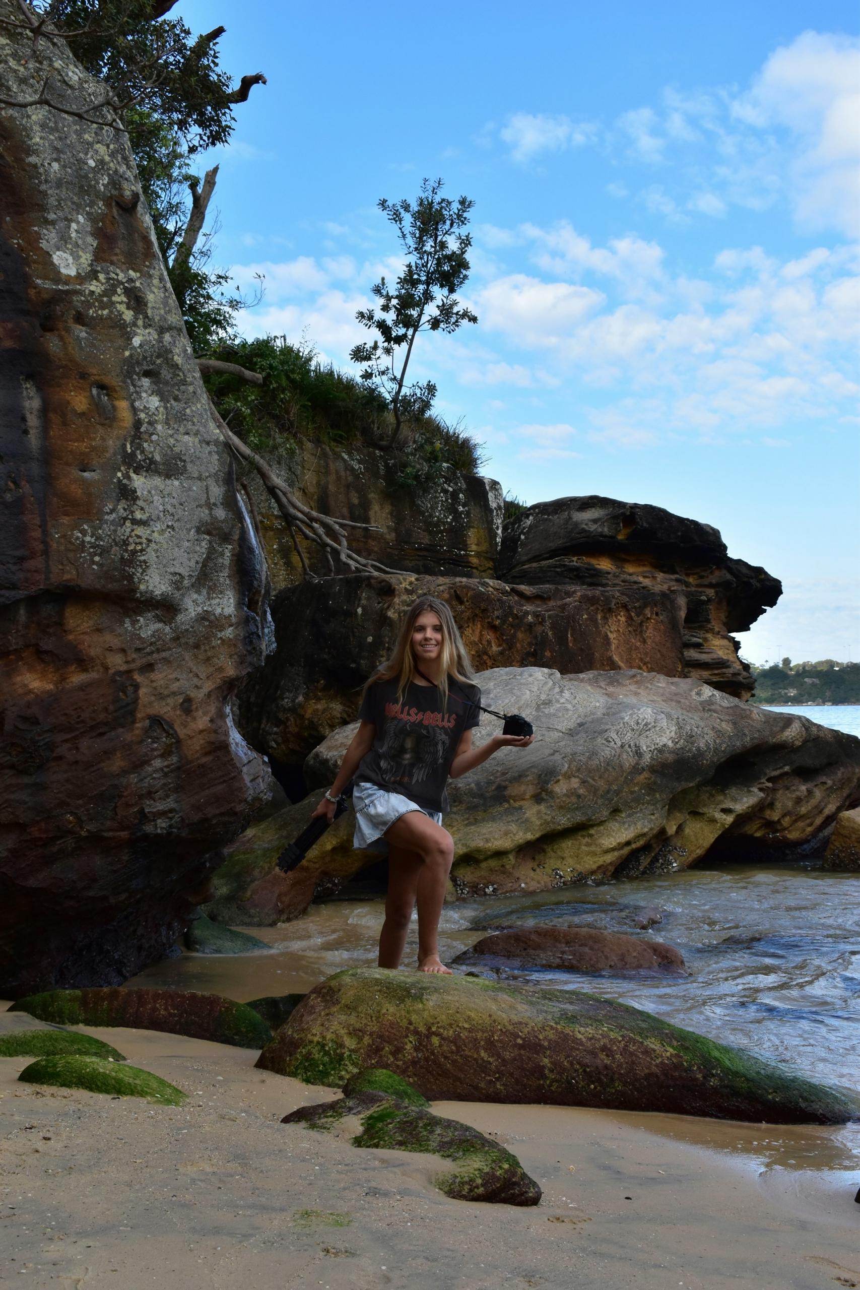 A woman stands on a beach in daylight. 