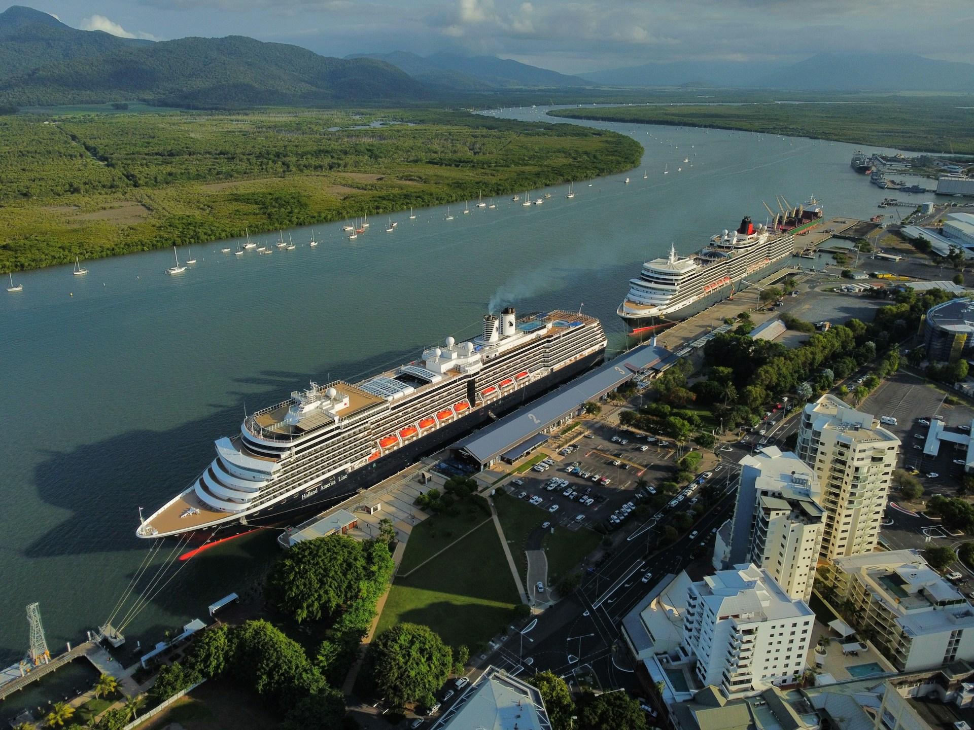An aerial view of two cruise ships docked at a city's port on a sunny day. 