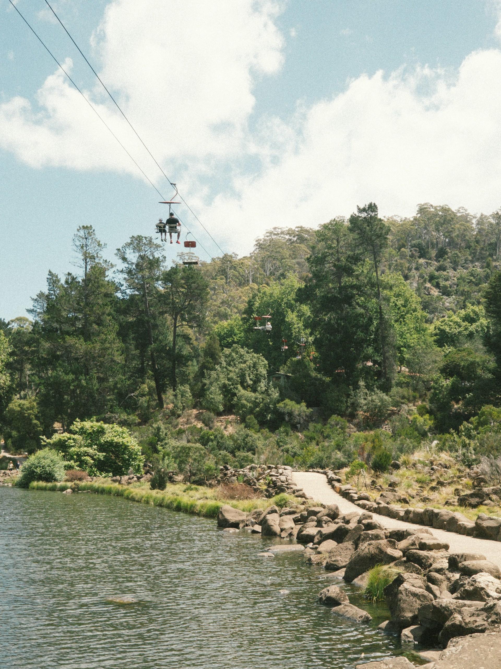A chairlift gliding across a body of water on a cloudy day. 
