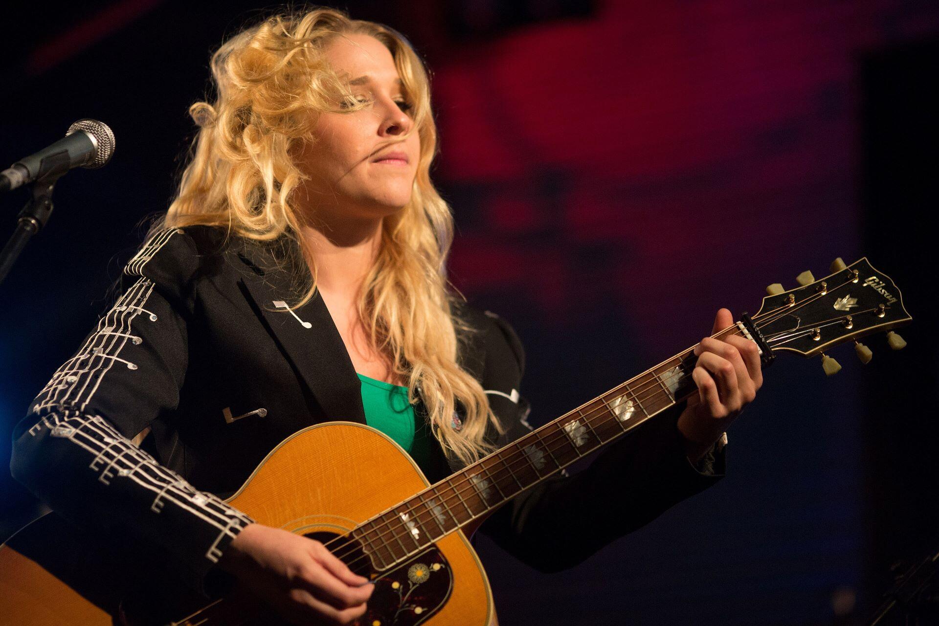 Catherine Britt playing an acoustic guitar beside a microphone during a live performance.