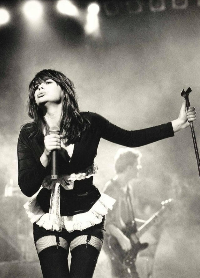 Black and white photo of Chrissy Amphlett performing on stage in her iconic French maid outfit