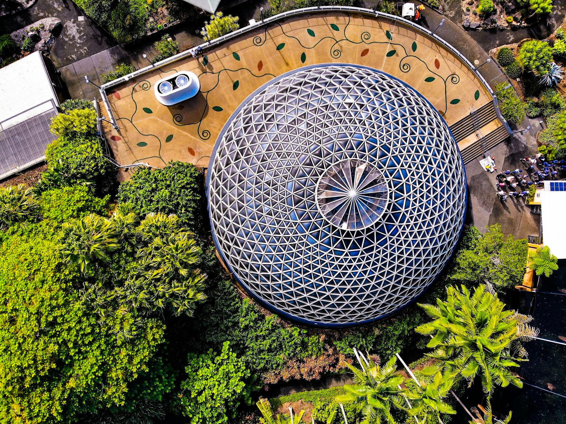 An aerial view of a round buildinng surrounded by trees on a sunny day.