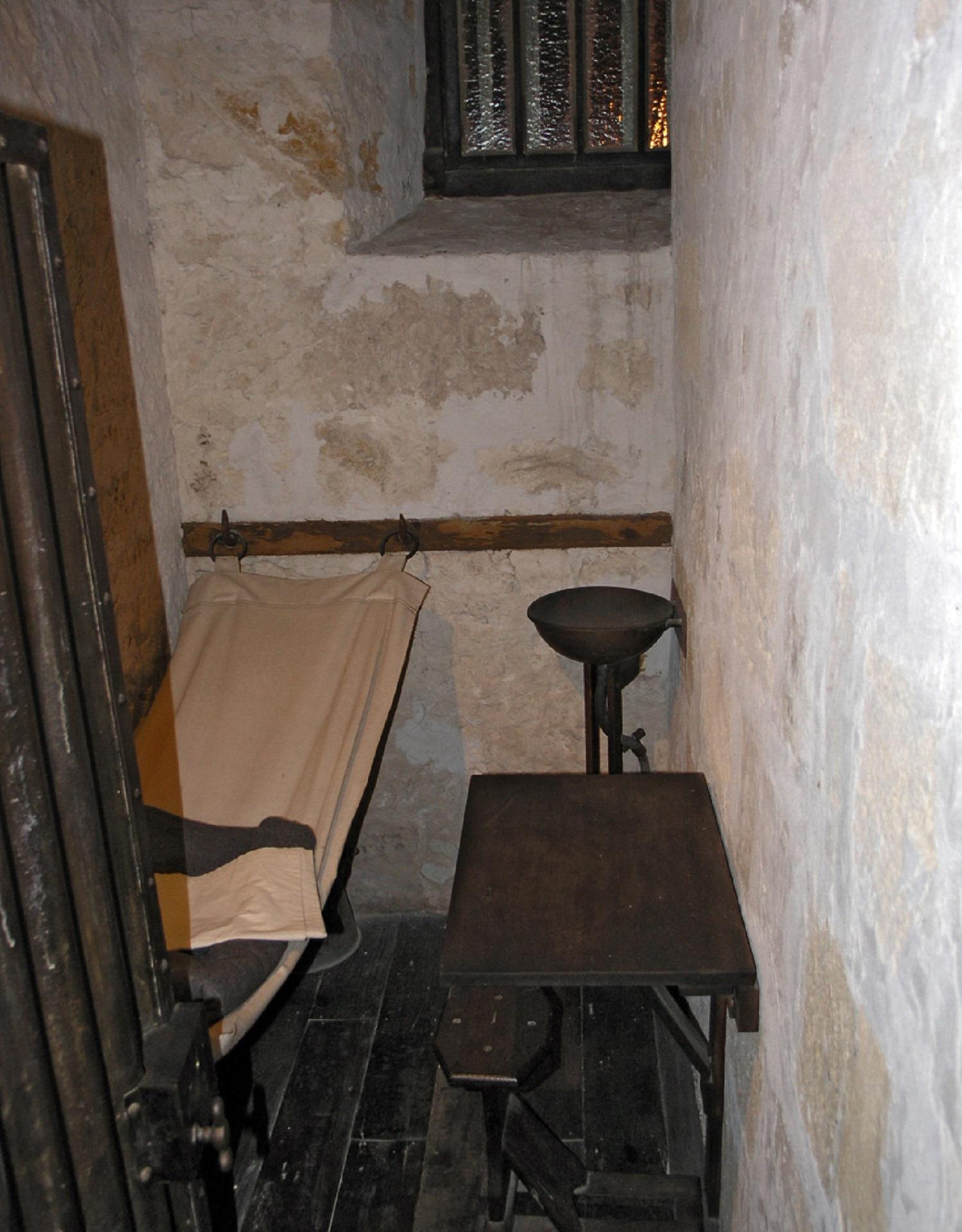 A narrow room with a bunk, sink and table. 