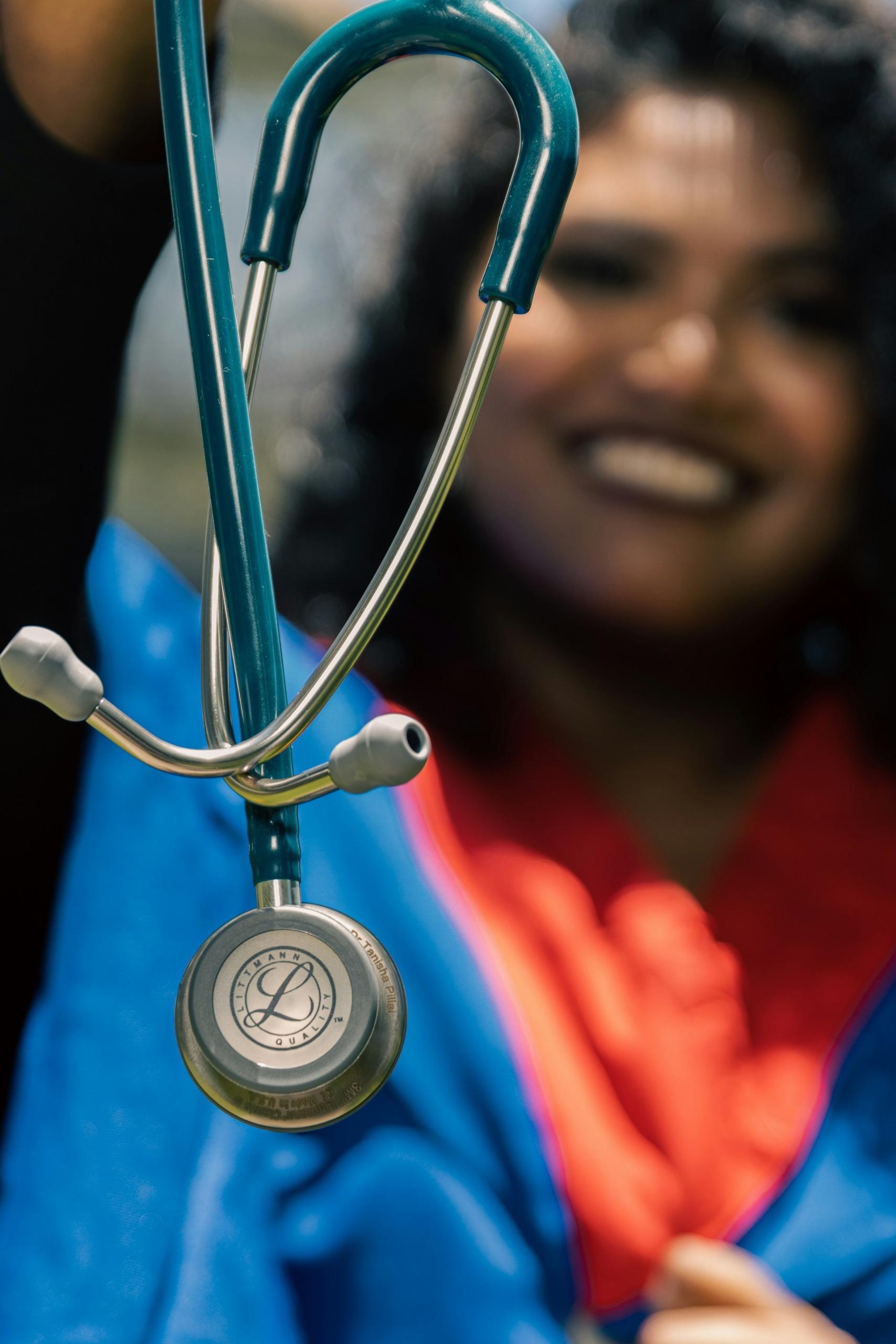 A woman wearing blue holds up a stethoscope. 