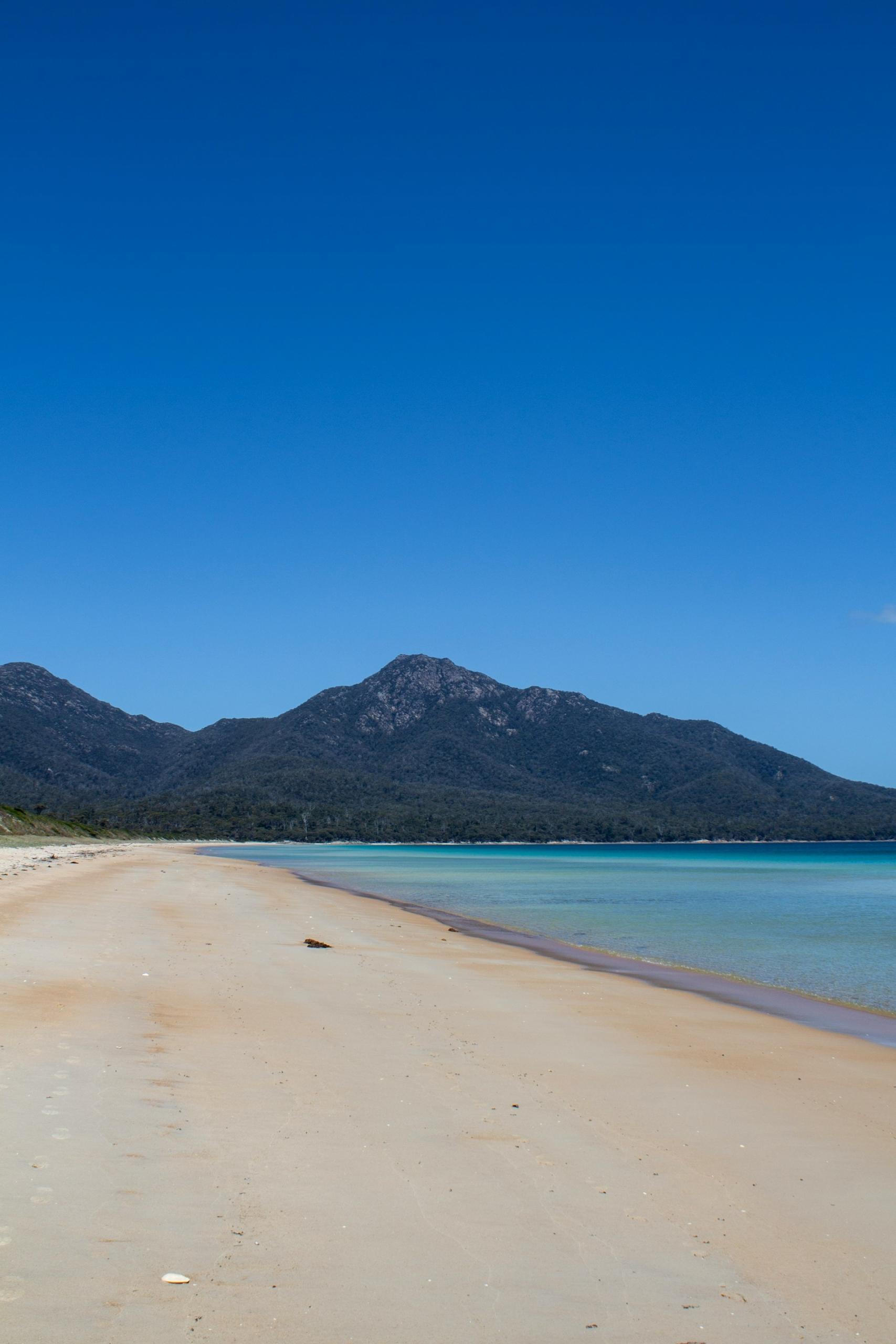 A strand and a mountain range in the background on a sunny day. 