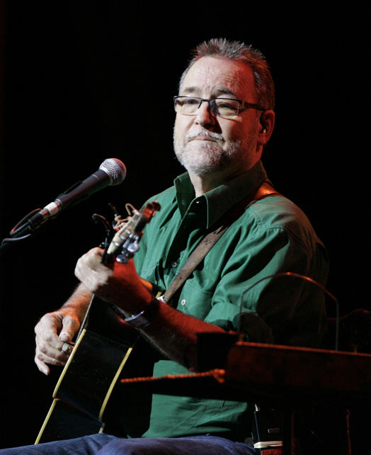 John Williamson playing guitar on stage, wearing a green shirt