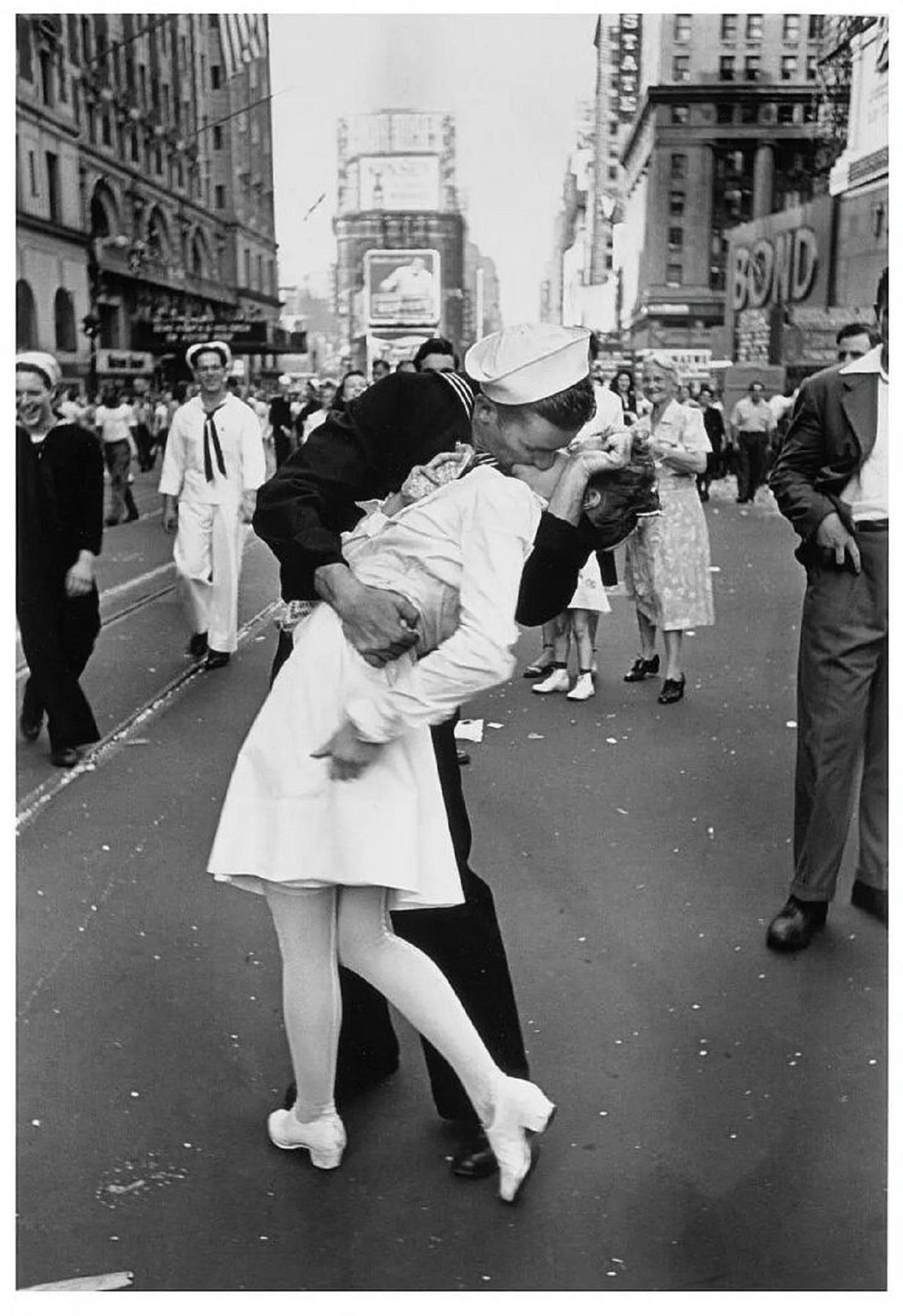 A greyscale image of a man kissing a woman on the street.