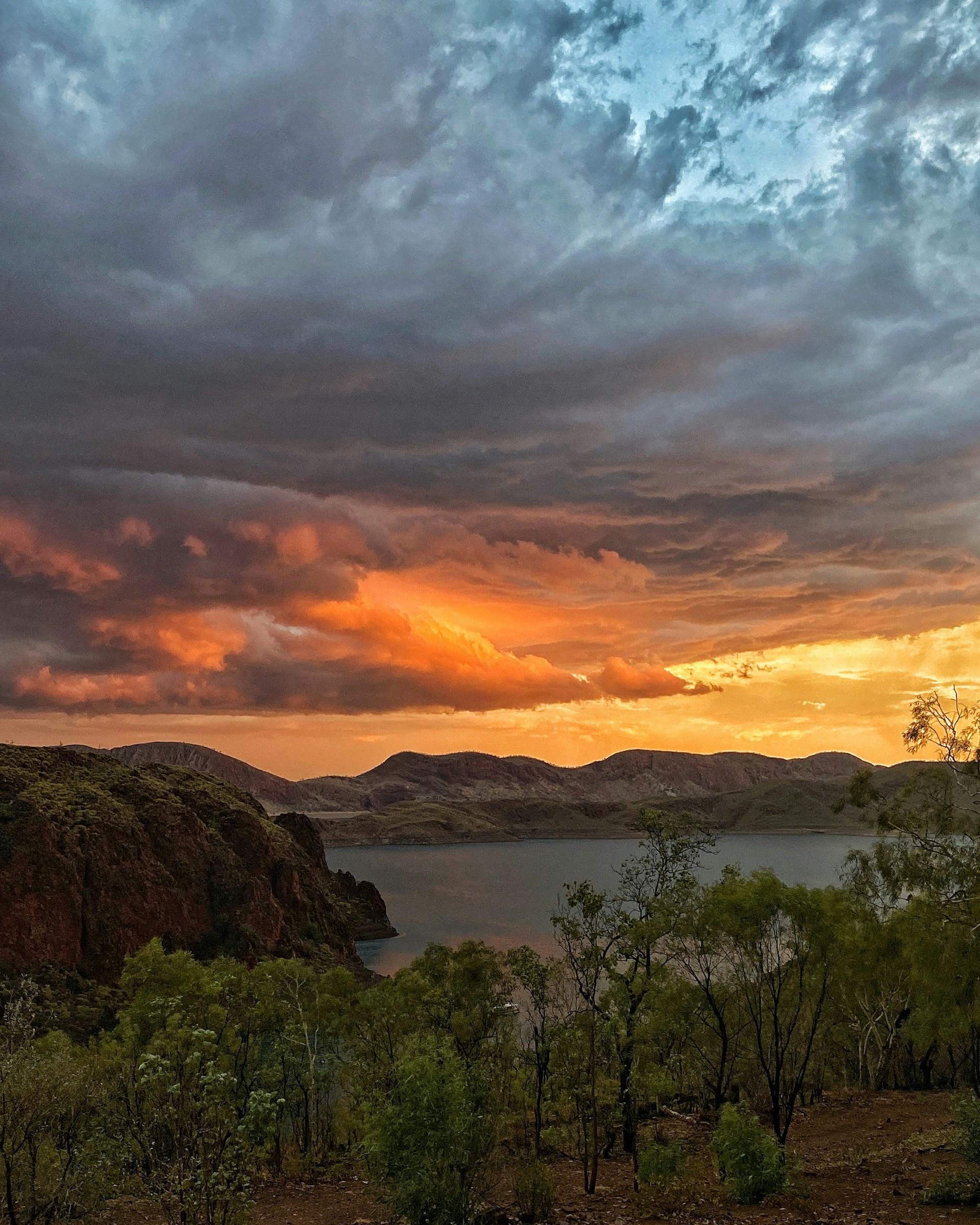 A lake and vegetation under cloudy skies at sunset. 