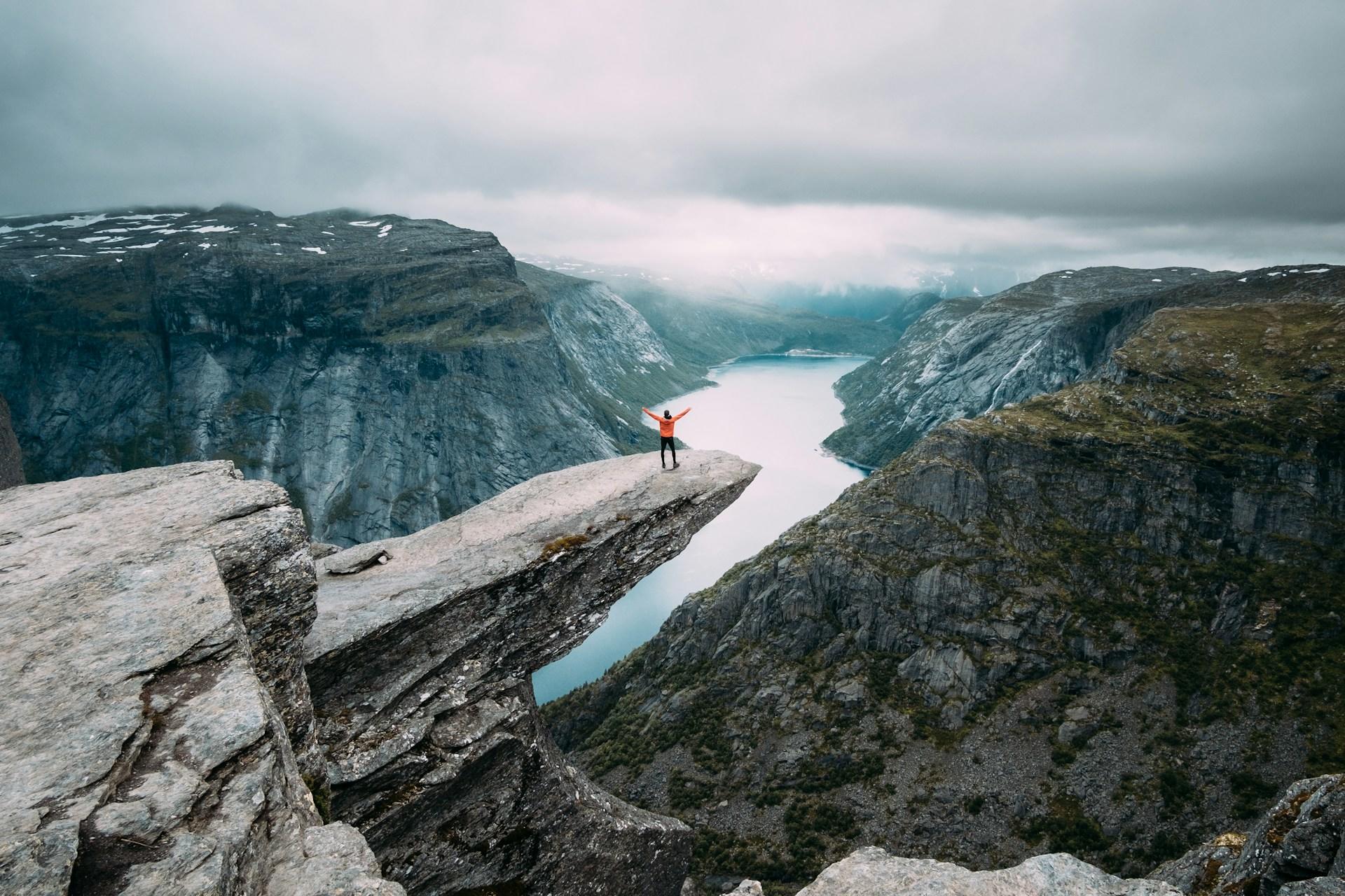 A person standing on a cliff, overlooking a river.